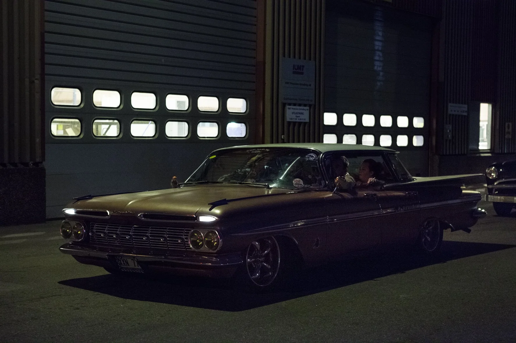 Une voiture classique noire stationnée devant une porte de garage en acier.