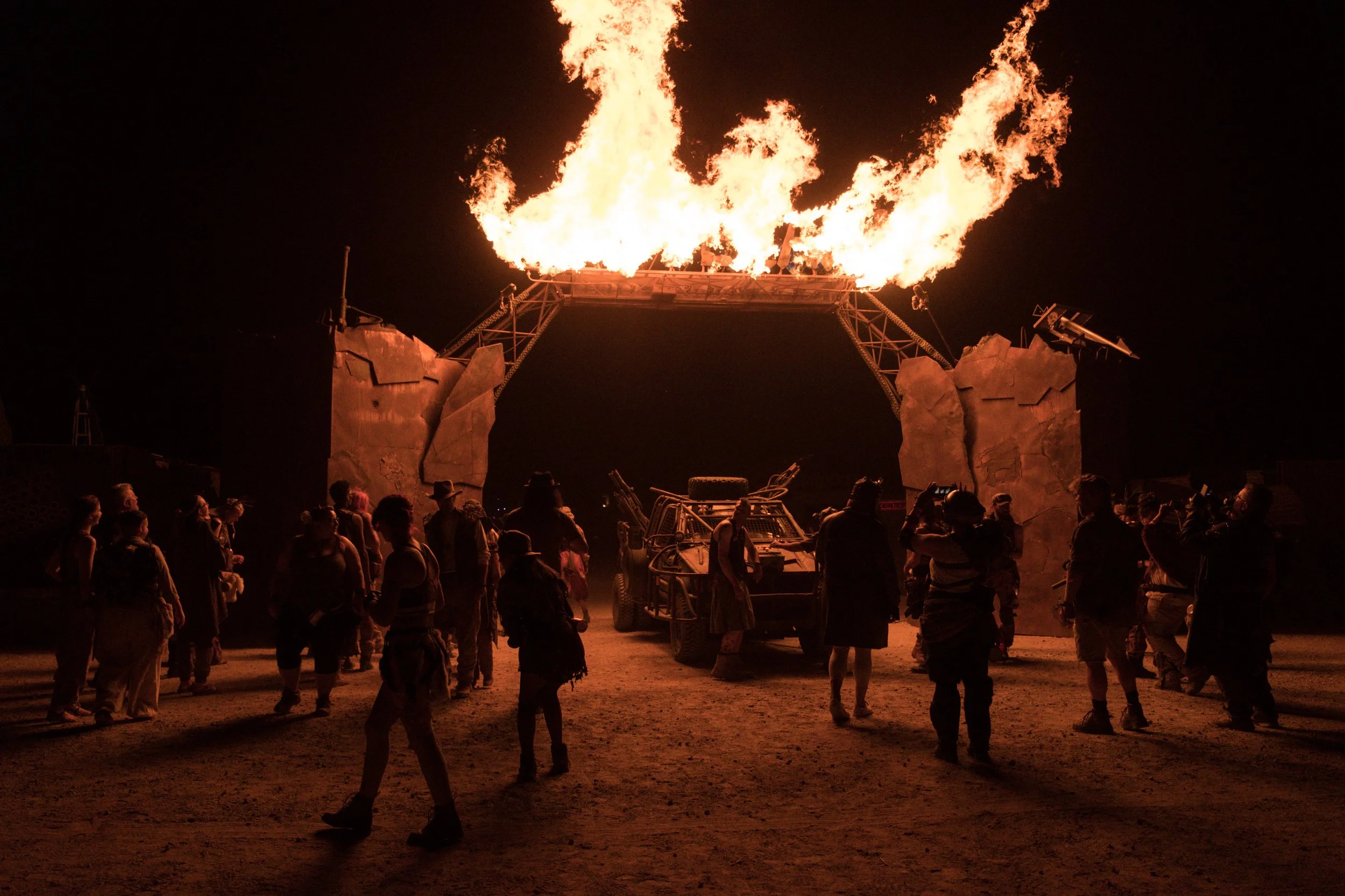 Un groupe de personnes regarde un arche en plein air dans le désert du Nevada où un grand feu est allumé sur une structure métallique au festival Wasteland.