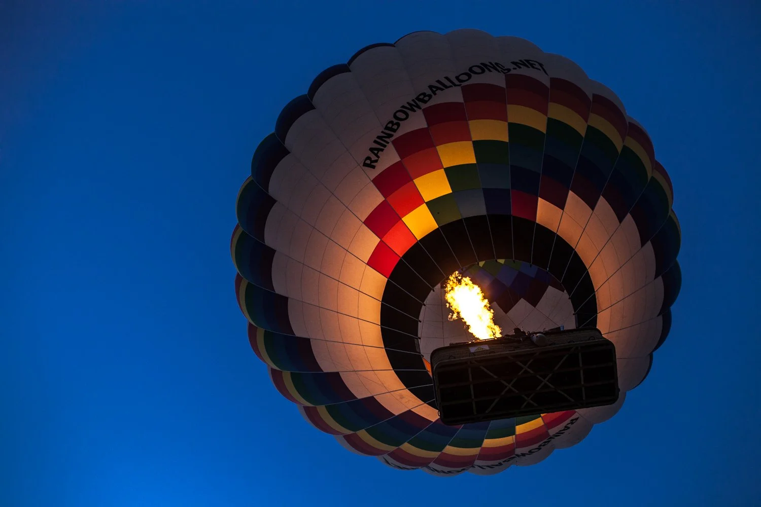 Montgolfière colorée en vol avec flamme dans le ciel bleu du matin.
