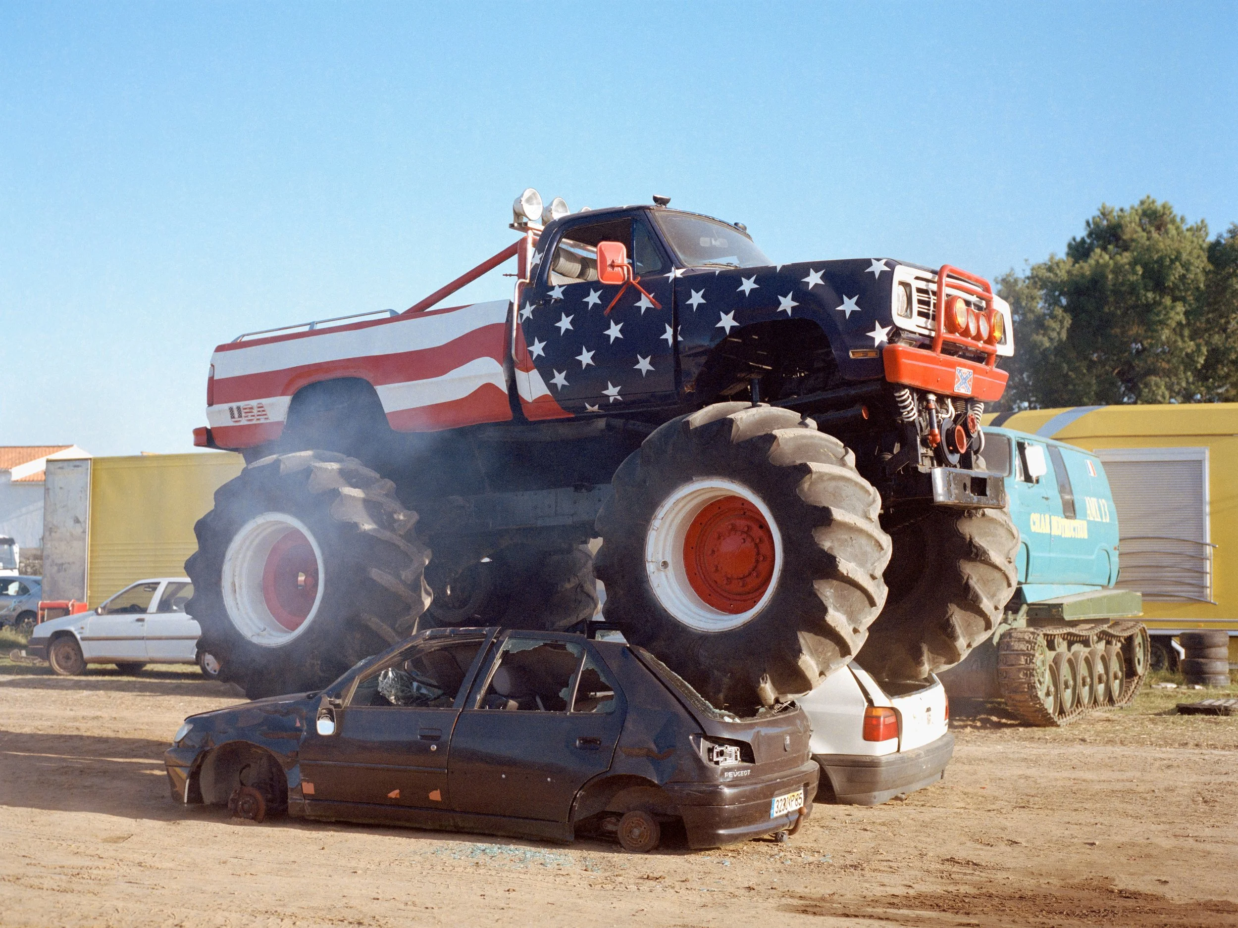 Un gigantesque Monster Truck avec la carrosserie peinte avec un motif de drapeau américain écrasant des voitures cassées, lors d'un show en Vendée.