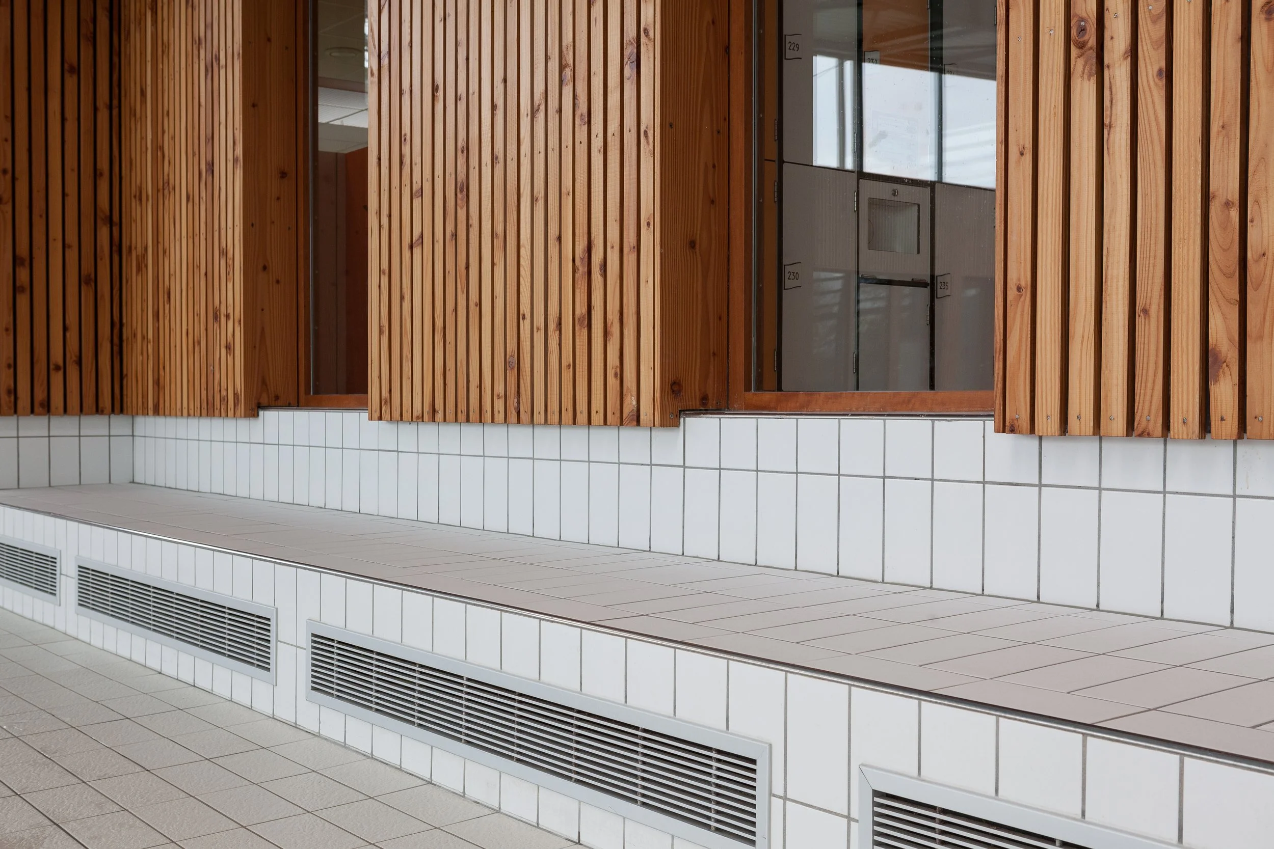 Mur en carrelage blanc et bois avec fenêtres en verre japonais et radiateurs sous la fenêtre dans une pièce neutre.