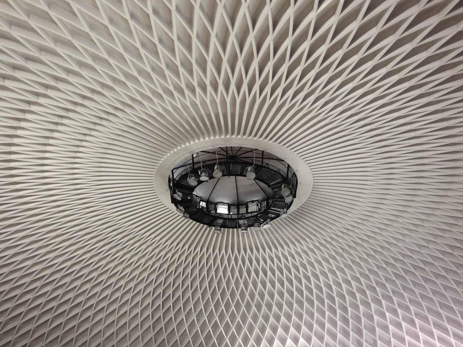 Vue du plafond d'un gymnase à Porto en formes géométriques blanches en spirale avec un centre circulaire contenant des lampes et une plateforme noire.