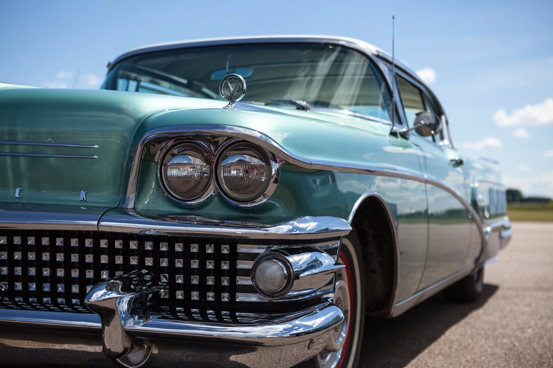 Voiture ancienne de couleur vert menthe avec des détails en chrome, photographie prise lors d'une journée ensoleillée.