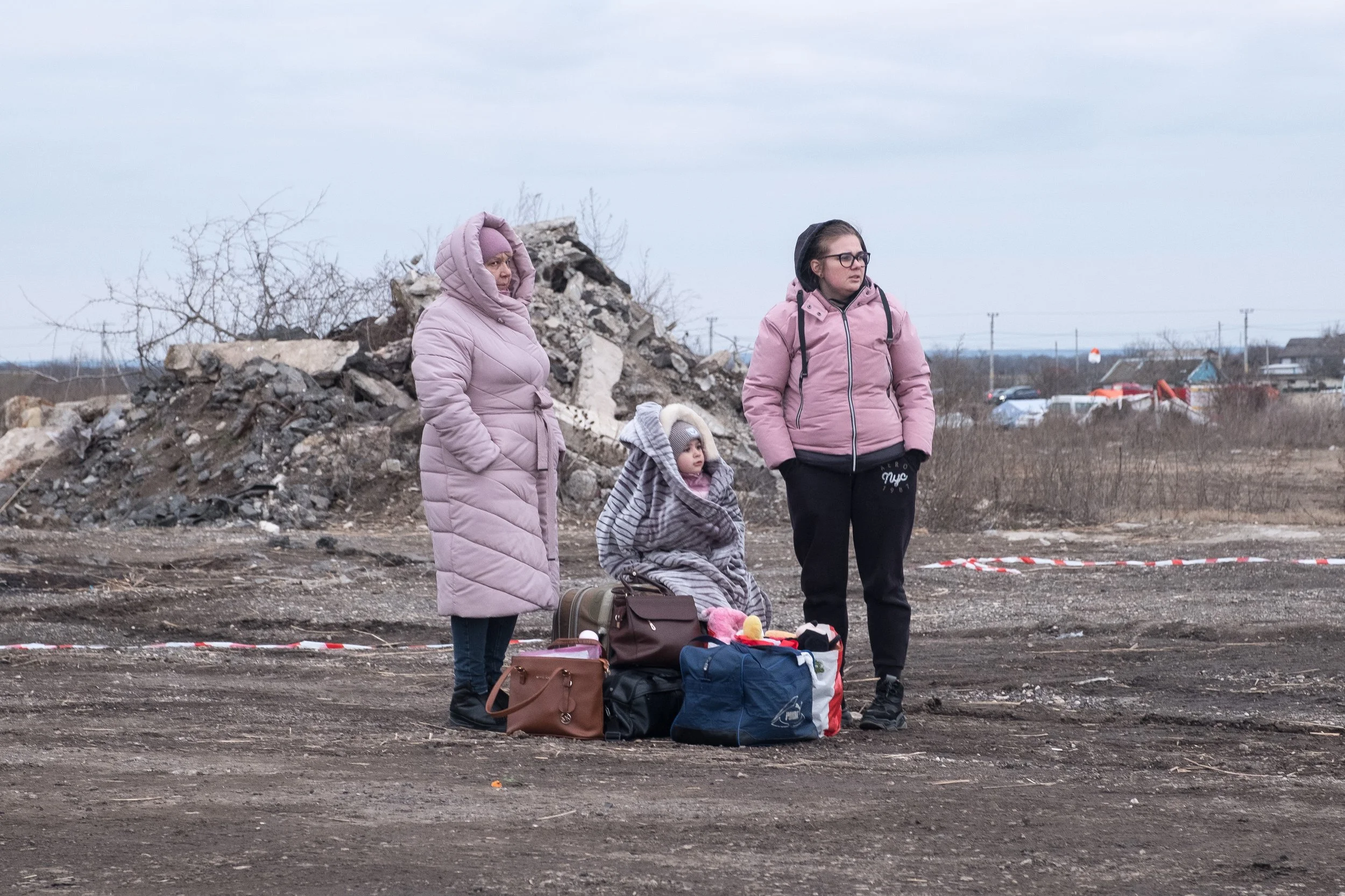 Trois ukrainiennes et un enfant avec des bagages en terrain accidenté, à la frontière moldave juste après le début de la guerre, en plein jour avec un ciel nuageux.