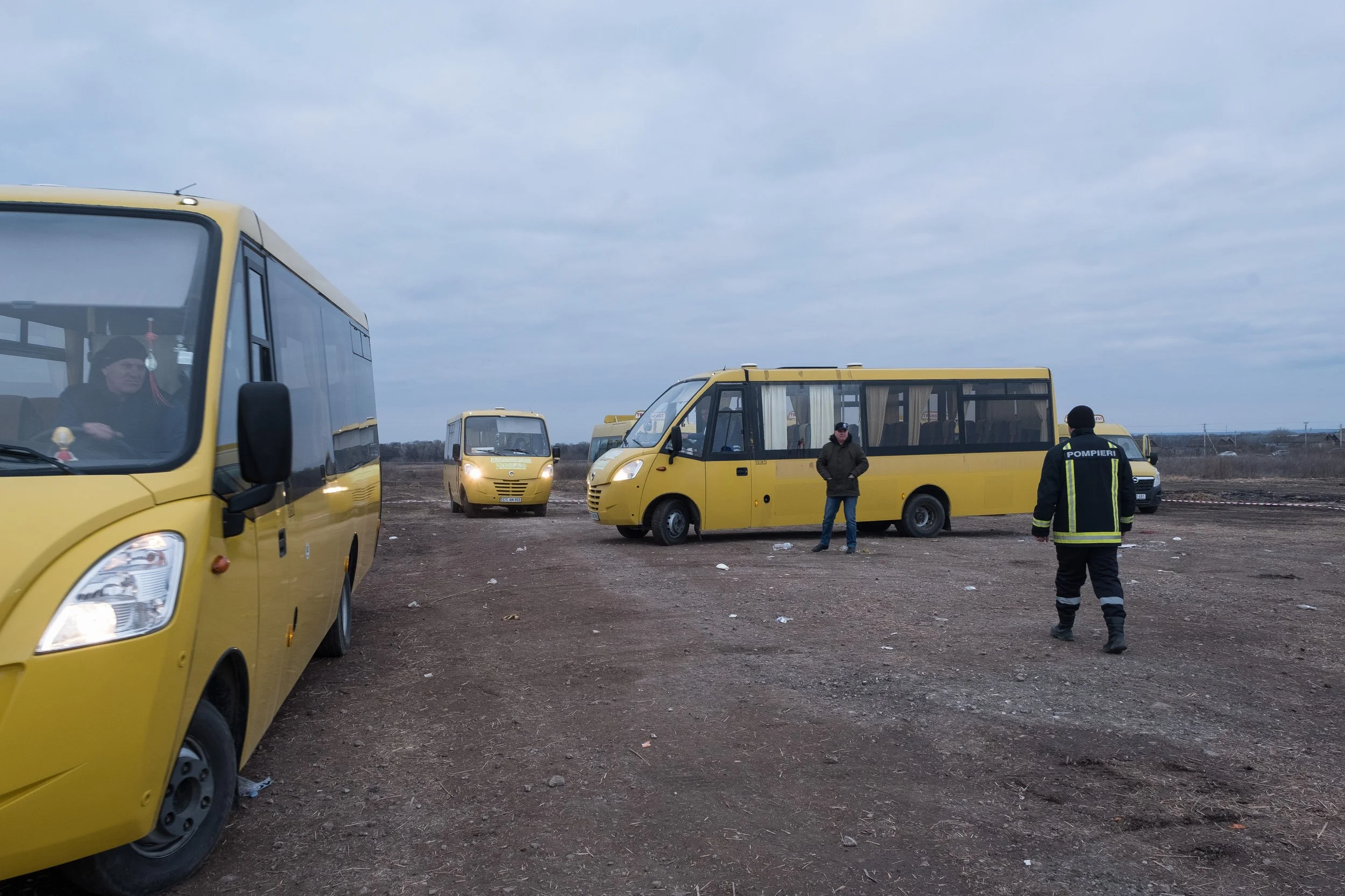 Un terrain en Moldavie avec plusieurs bus jaunes, quelques personnes dont un pompier en uniforme. Le ciel est nuageux.