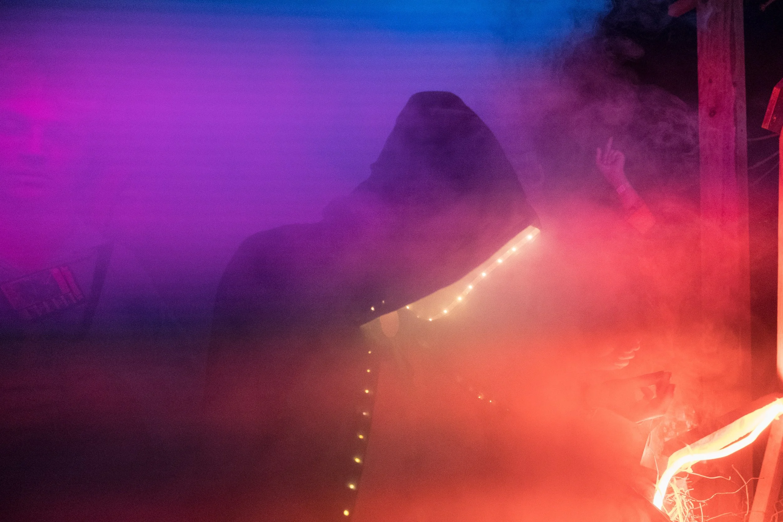 Une personne avec un hoodie dans une ambiance sombre et brumeuse, éclairée par des lumières colorées et une lumière rouge intense au festival Lapiñata.