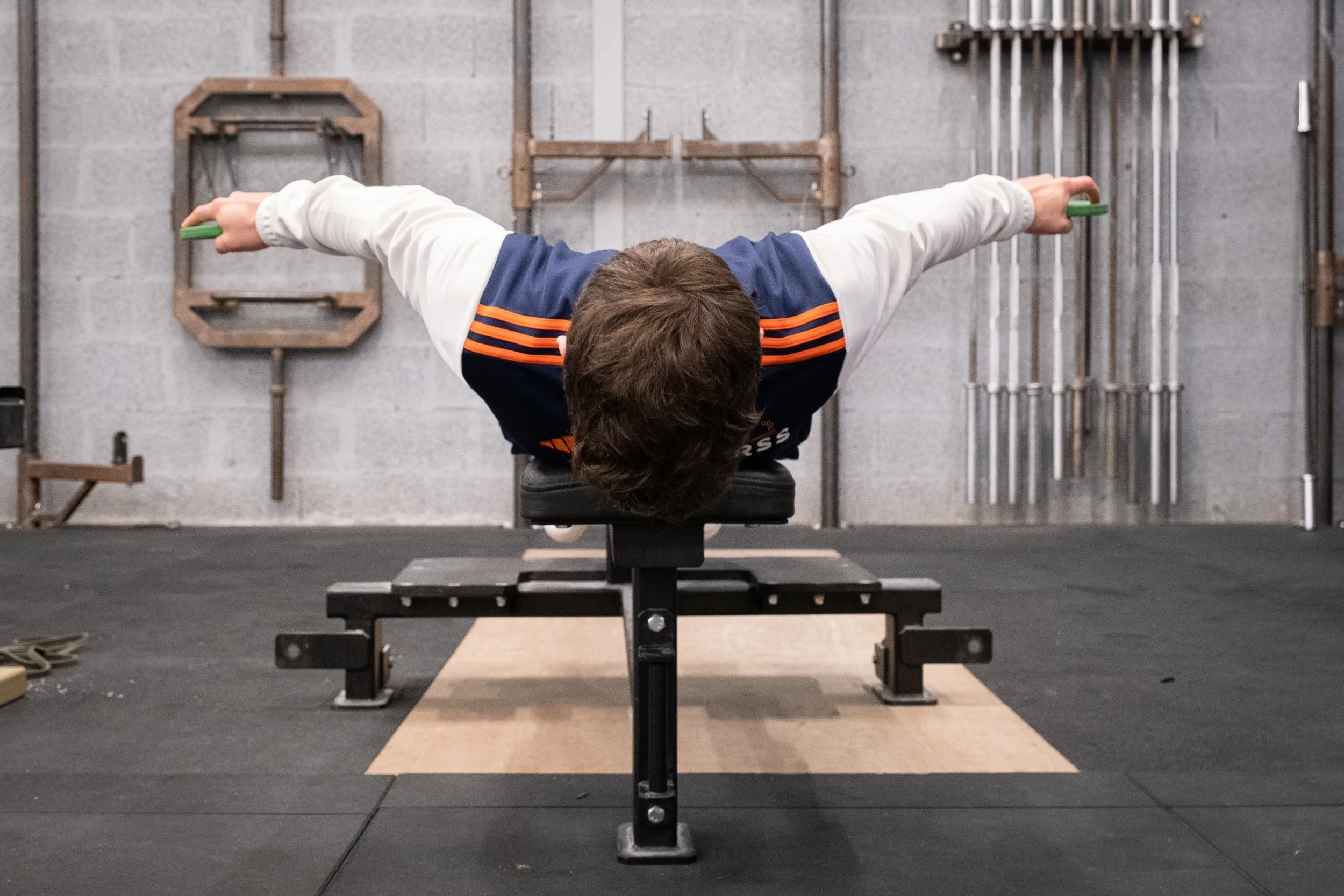 Homme faisant un exercice d'étirement ou de musculation allongé sur un banc avec les bras étendus horizontalement, dans une salle de sport