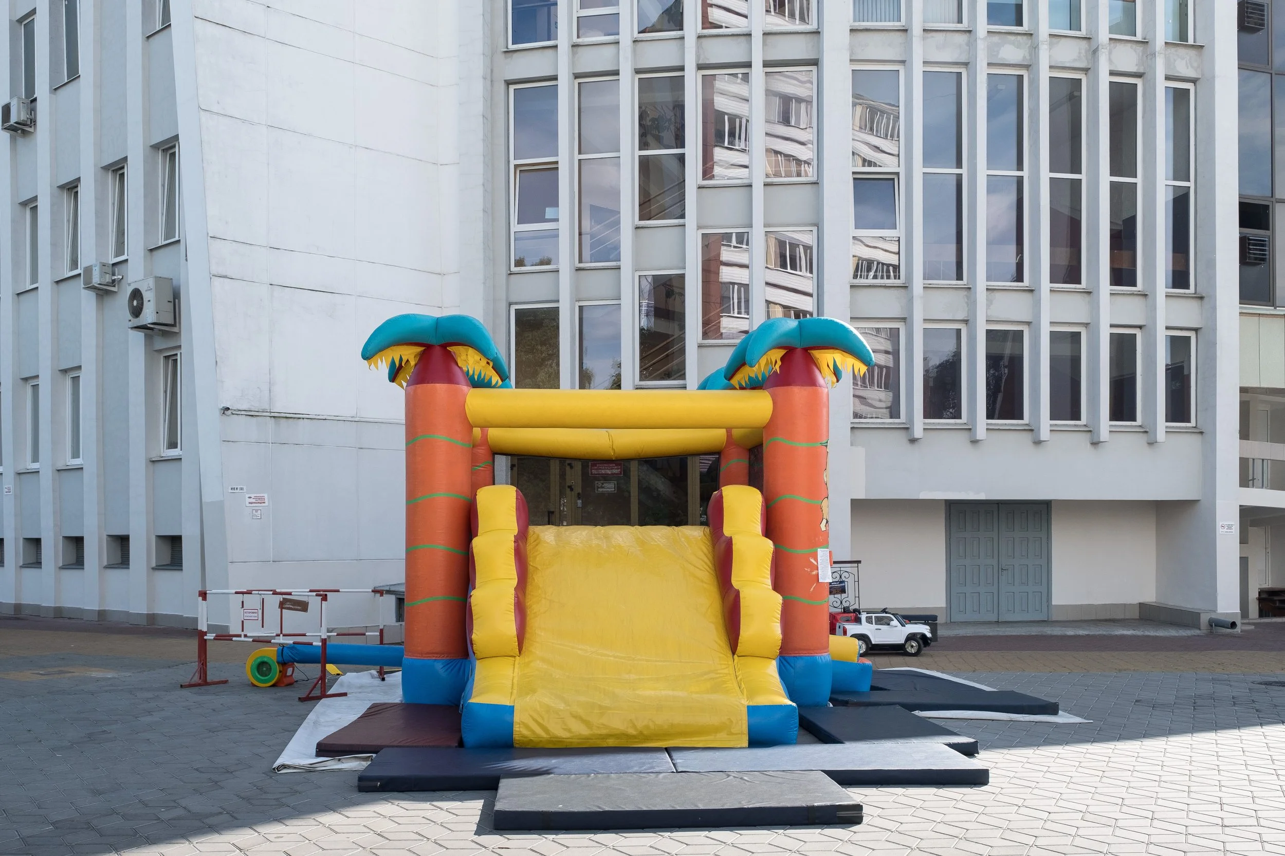 Structure gonflable pour enfants avec toboggan, décorée en couleurs vives, installée devant un bâtiment moderne avec des fenêtres en verre.