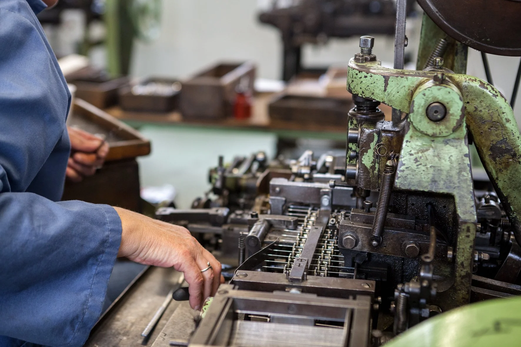 Un atelier de fabrication d'aiguilles avec une personne manipulant une machine ancienne en métal vert.