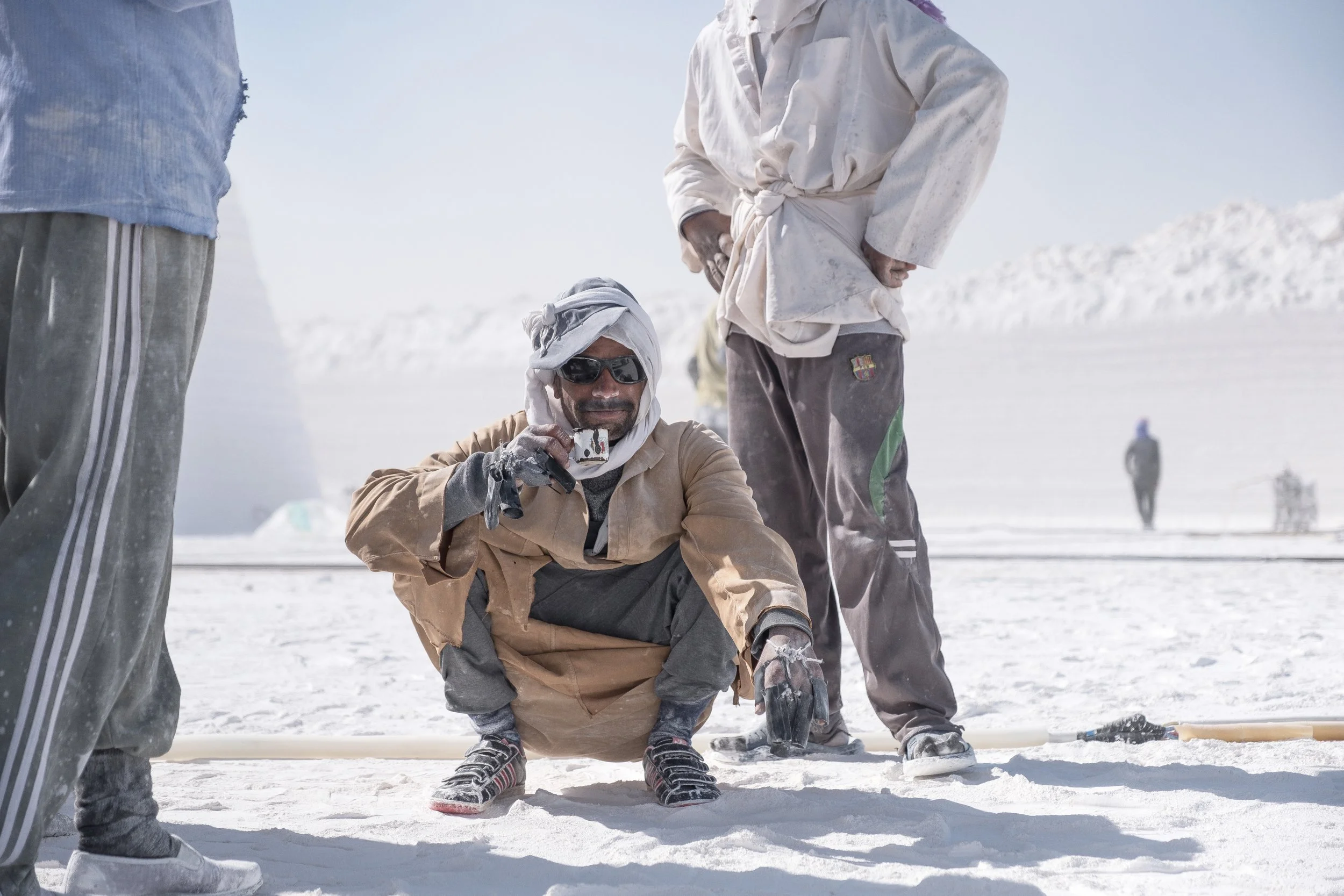 Homme buvant du thé dans un environnement blanc, et portant une djellaba, avec un ciel clair en arrière-plan.