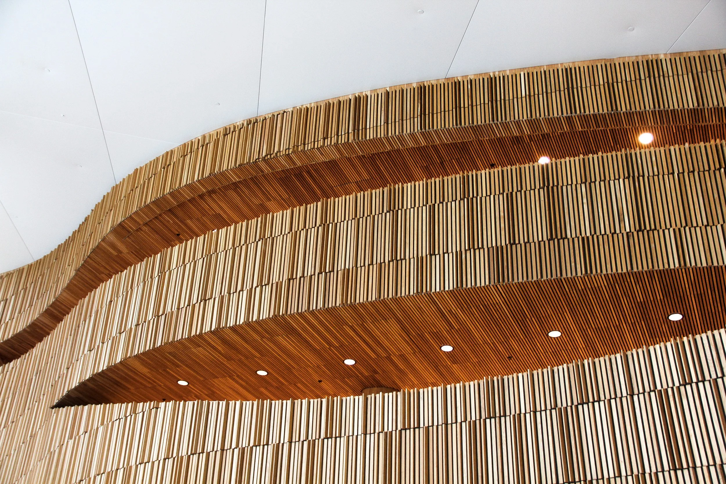 Structure intérieure de l'opéra d'Oslo de Snøhetta avec murs en bois sculpté en formes ondulantes, plafond blanc et lumières encastrées.