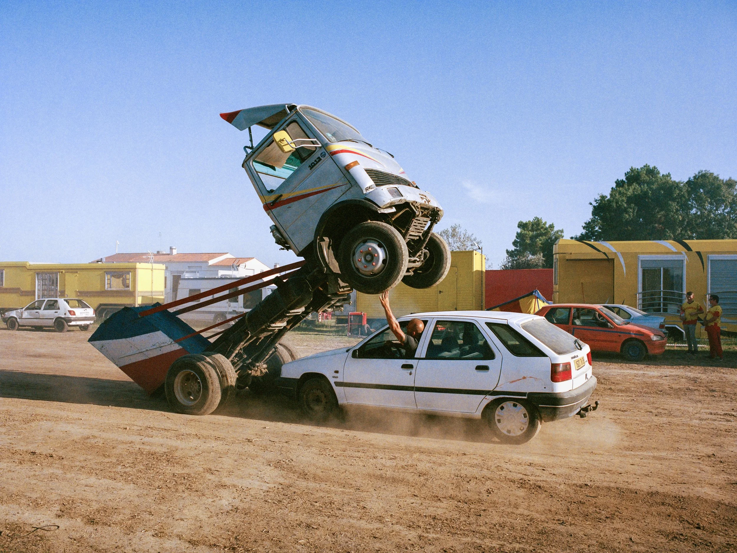 Un camion se cabrant au-dessus d'une voiture lors d'un show de Monster Truck, avec des personnes regardant en arrière-plan.