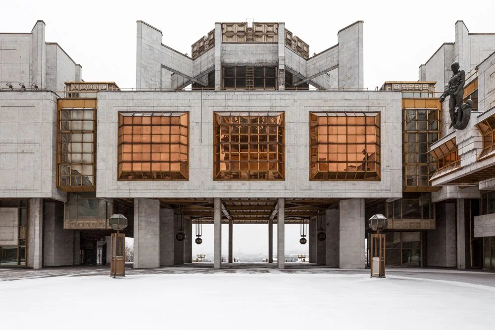 Image d'un bâtiment moderne en pierre blanche avec des fenêtres en verre teinté orange et des sculptures murales en bronze à Moscou.
