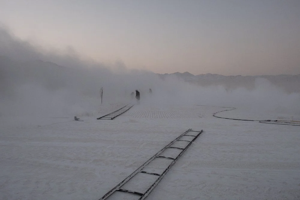 Paysage désertique avec des échelles en métal à plat sur le sol, brouillard ou vapeur recouvrant la scène, montagnes à l'horizon.