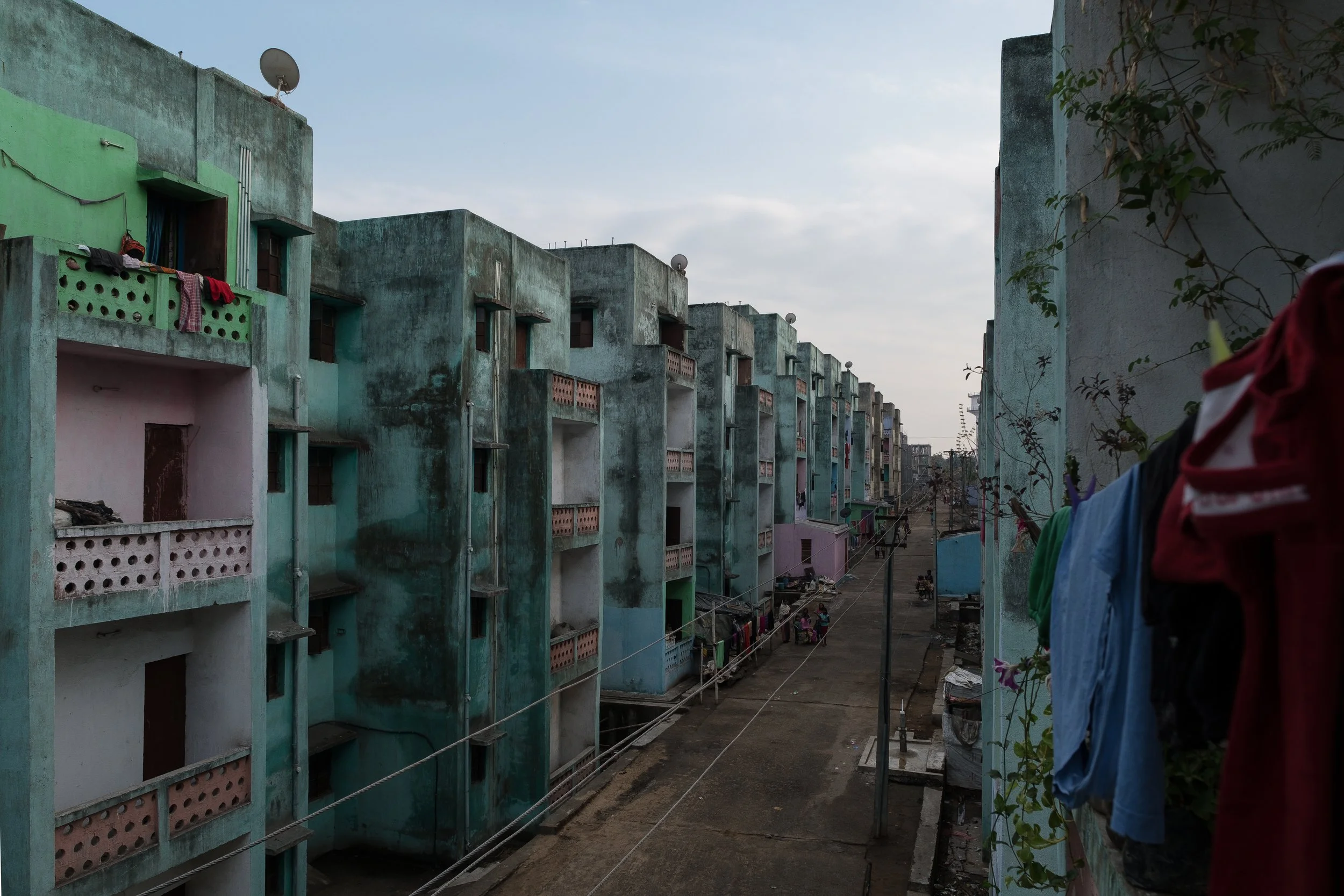 Vue d'une rangée d'immeubles colorés en pastel avec des balcons, certains avec des vêtements suspendus entre deux bâtiments, dans un environnement urbain.