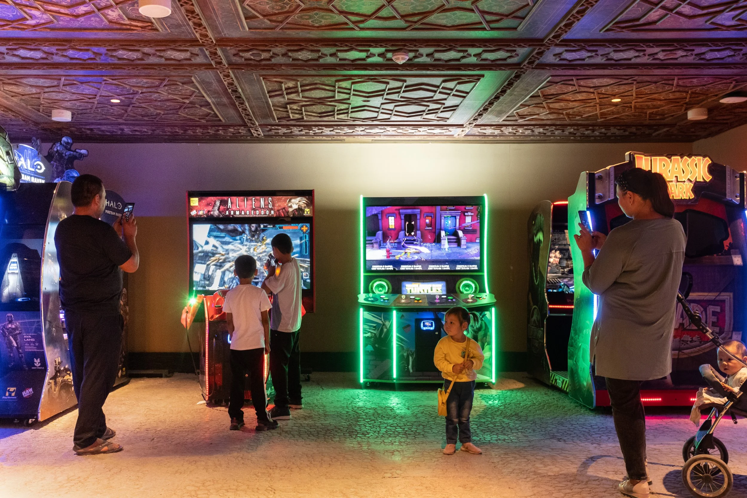 Enfants et adultes jouant à des jeux vidéo dans une salle de jeux d'arcade avec des machines illuminées, notamment un jeu d'Alien et un autre de Jurassic Park, à Turkestan au Kazakhstan.