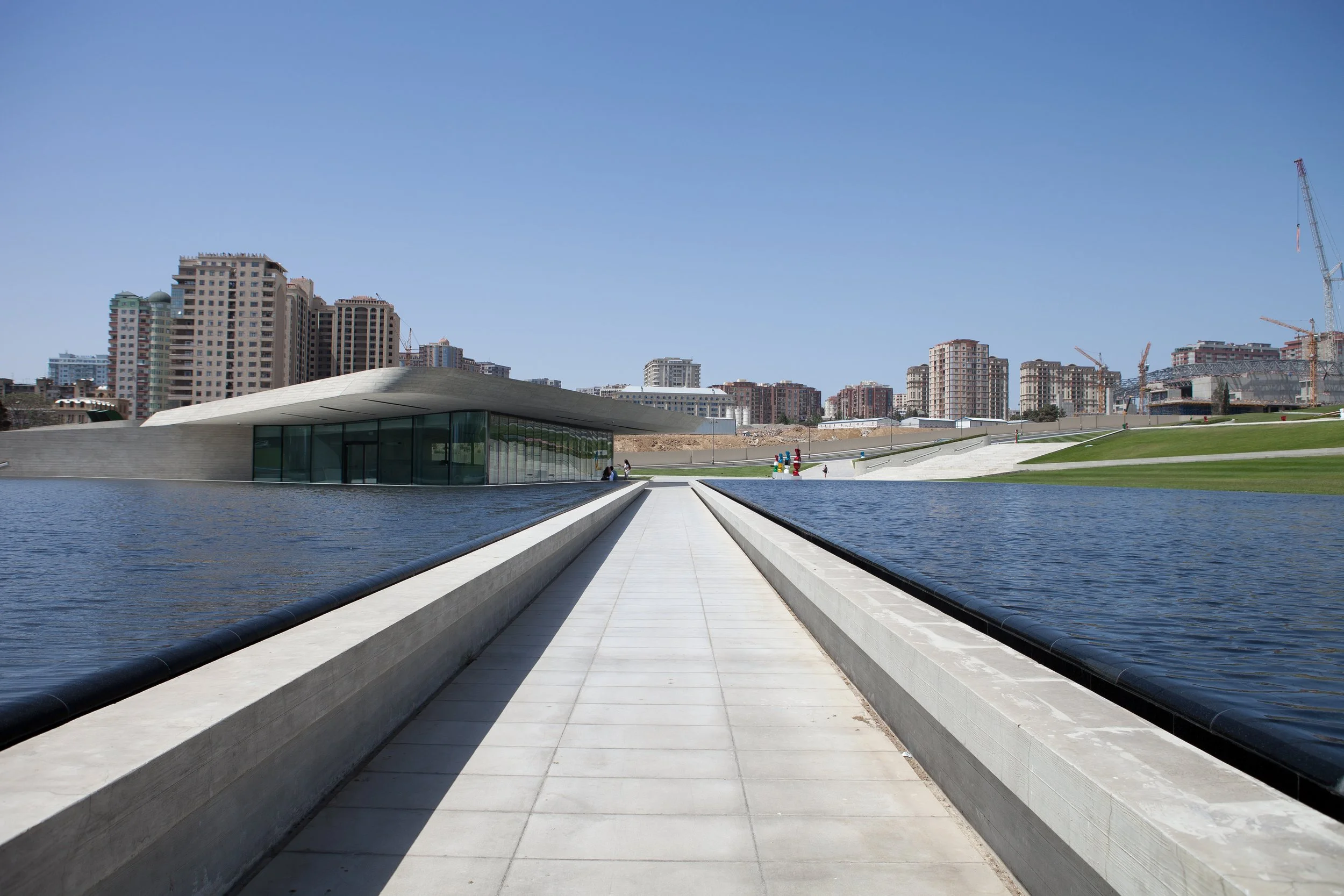 Vue de l'architecture moderne du centre Heydar Aliyev de Zaha Hadid à Baku, en Azerbaïdjan, avec des bassins et des bâtiments en arrière-plan, sous un ciel clair.