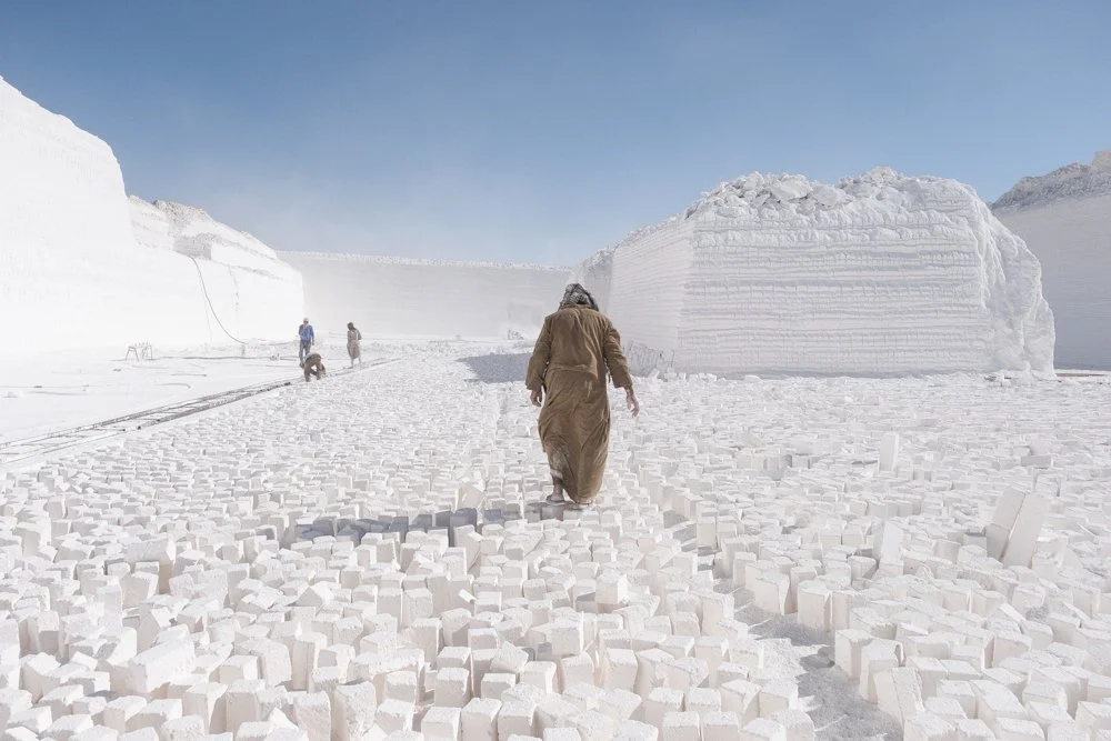 Travailleurs dans une grande carrière de calcaire avec des murs blancs en arrière-plan, le sol recouvert de blocs.