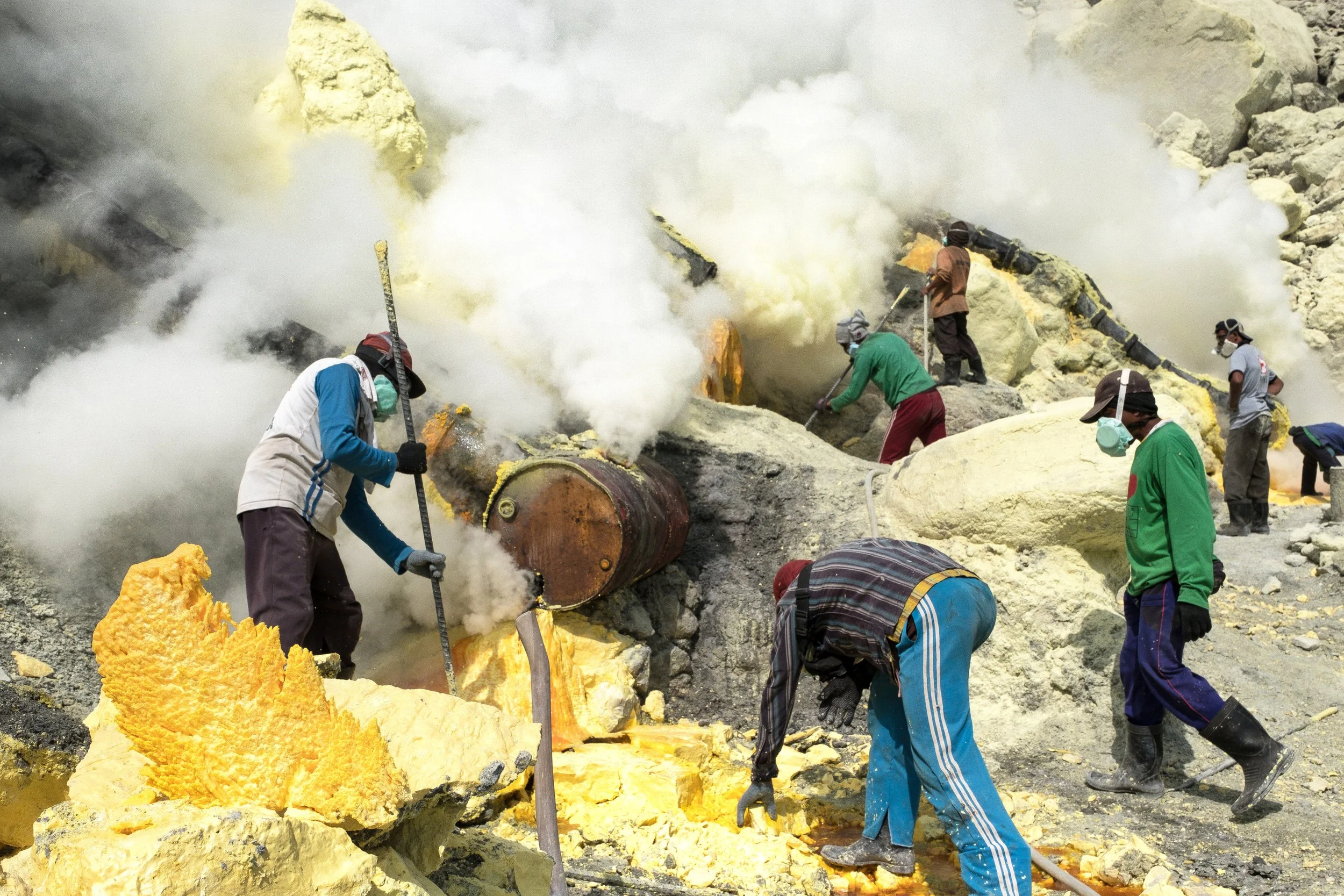 Des travailleurs portant des masques et des gants, utilisant des outils pour extraire du soufre jaune, avec beaucoup de vapeur et de fumée émanant du site d'extraction dans le volcan du Kawah Ijen.