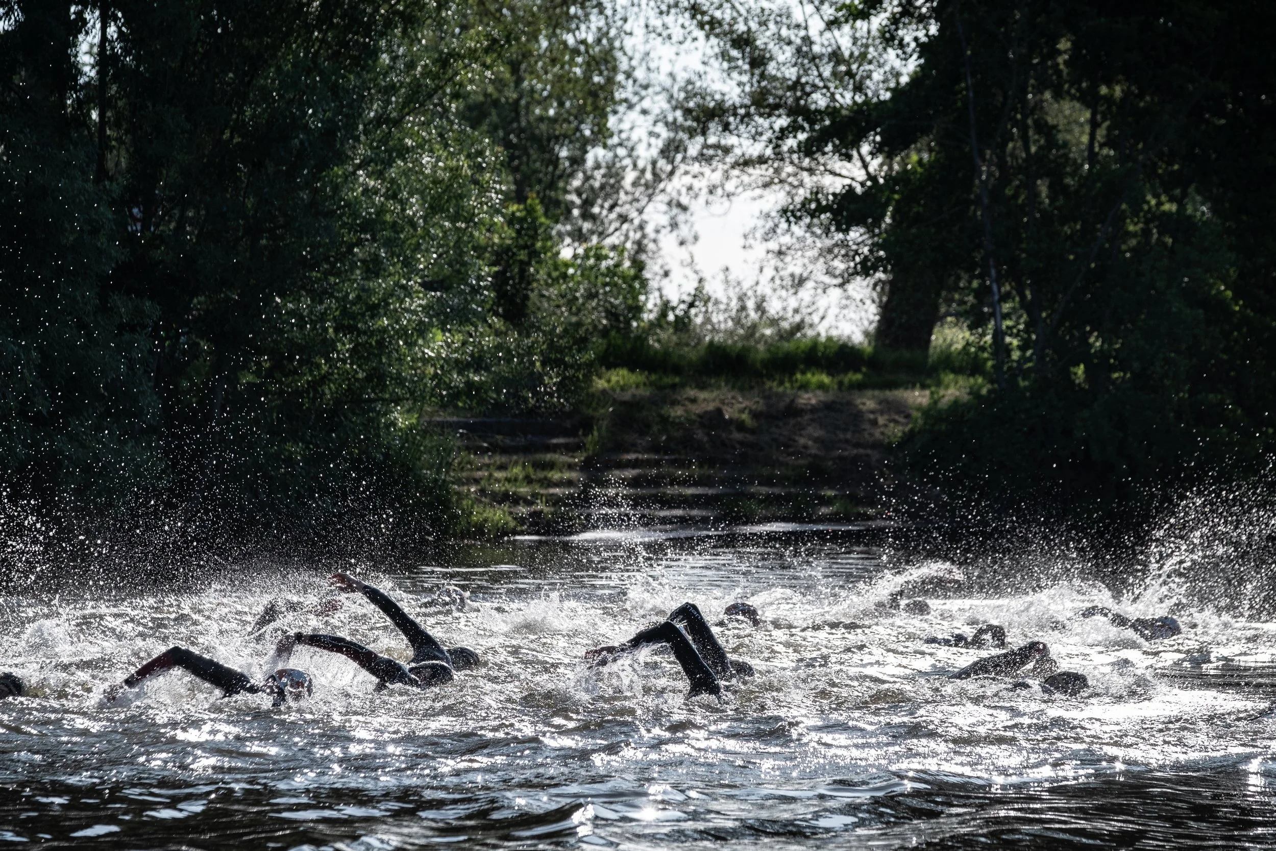 Baignade en eau vive avec plusieurs nageurs, forêt en arrière-plan.