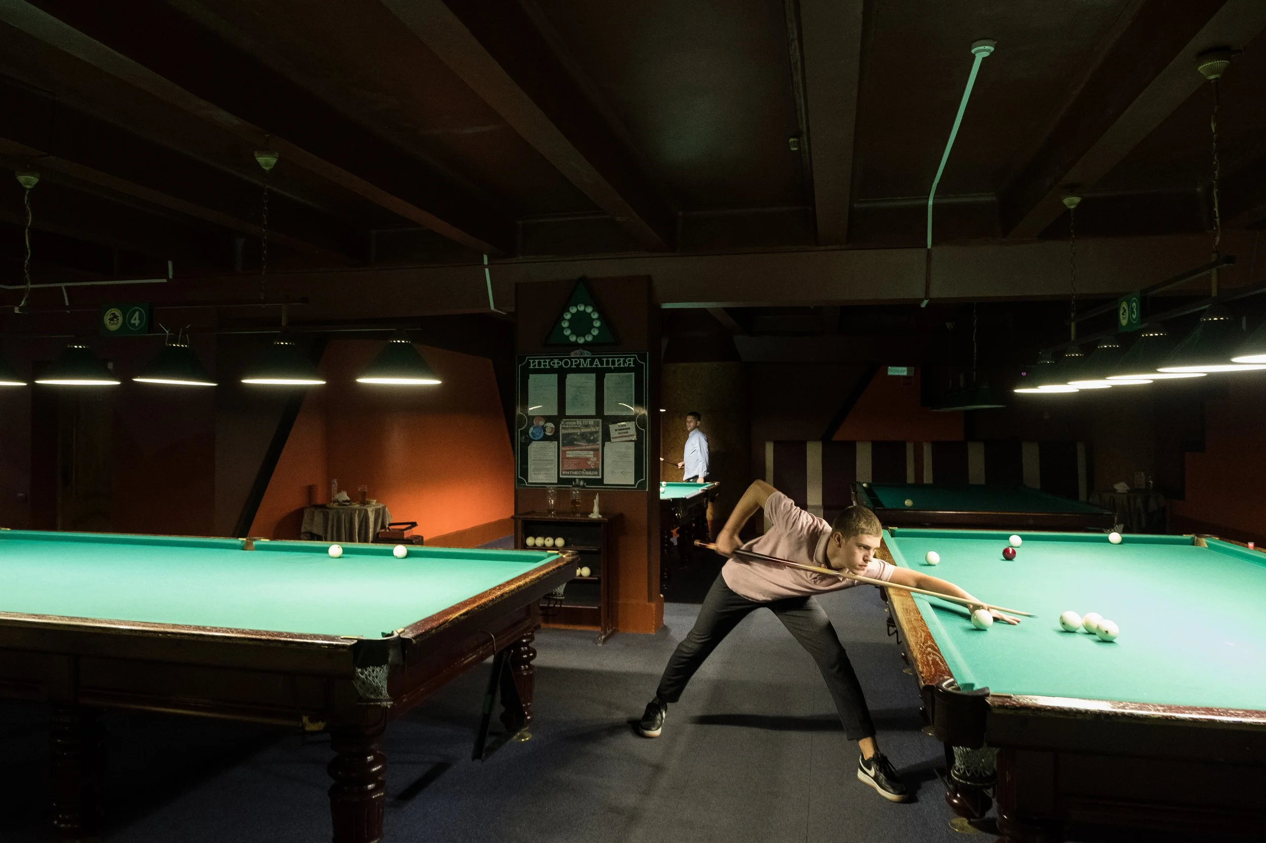 Un jeune homme joue au billard dans une salle de billard sombre éclairée par des lampes suspendues en Biélorussie.