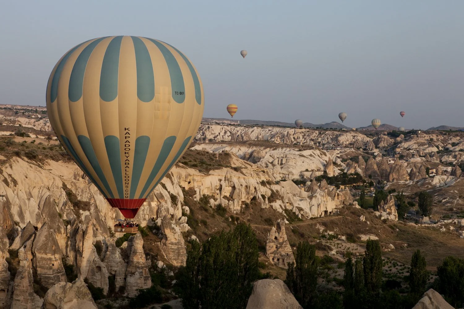 Plusieurs montgolfières en vol au-dessus d'un paysage rocheux et vallonné en Cappadoce, Turquie.