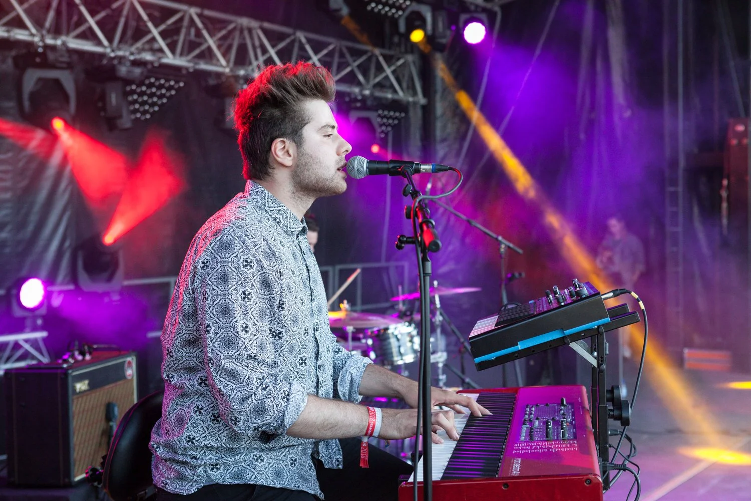 Un musicien joue du clavier sur scène lors d'un concert, avec des lumières colorées en arrière-plan.