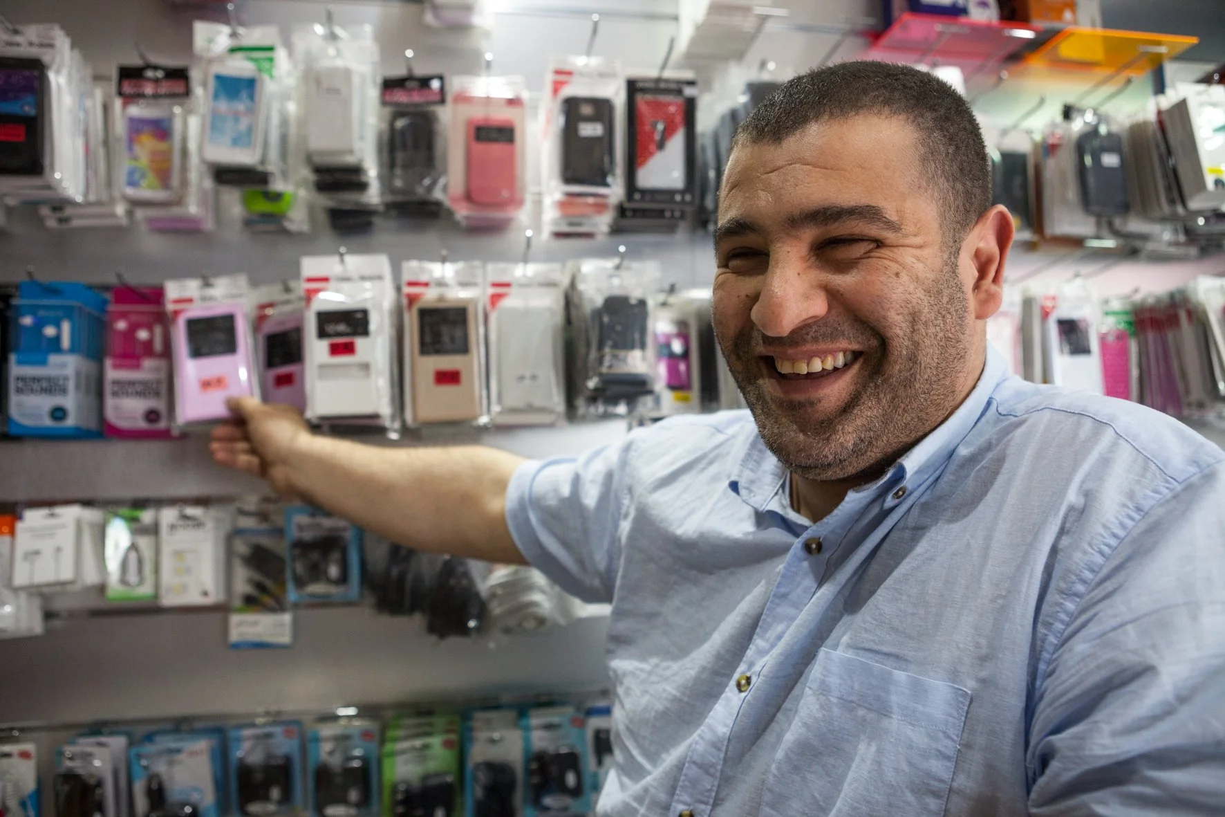 Un homme souriant dans un magasin d'accessoires pour téléphones, pointant vers une sélection de coques de téléphone exposées.