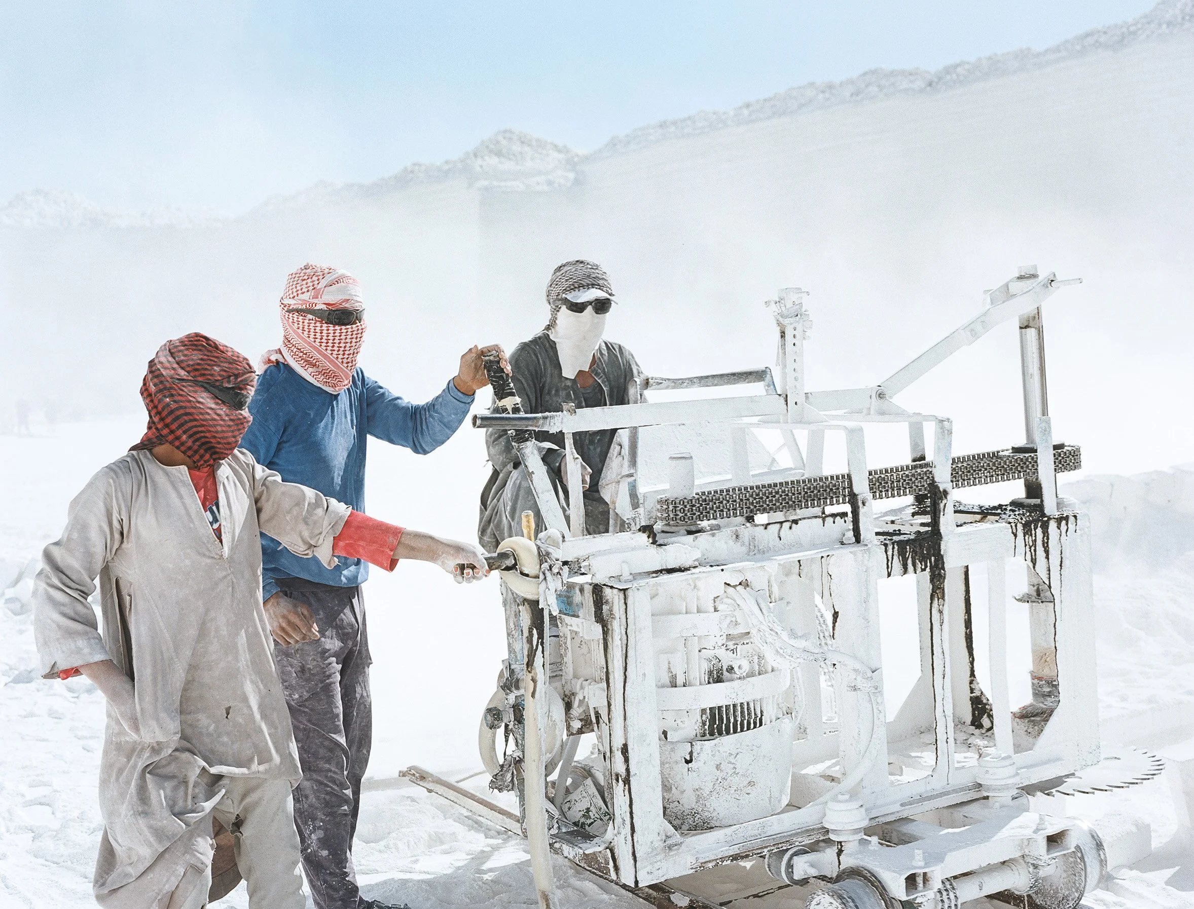 Quatre personnes masquées et habillées en vêtements traditionnels utilisent une machine dans un environnement blanc.