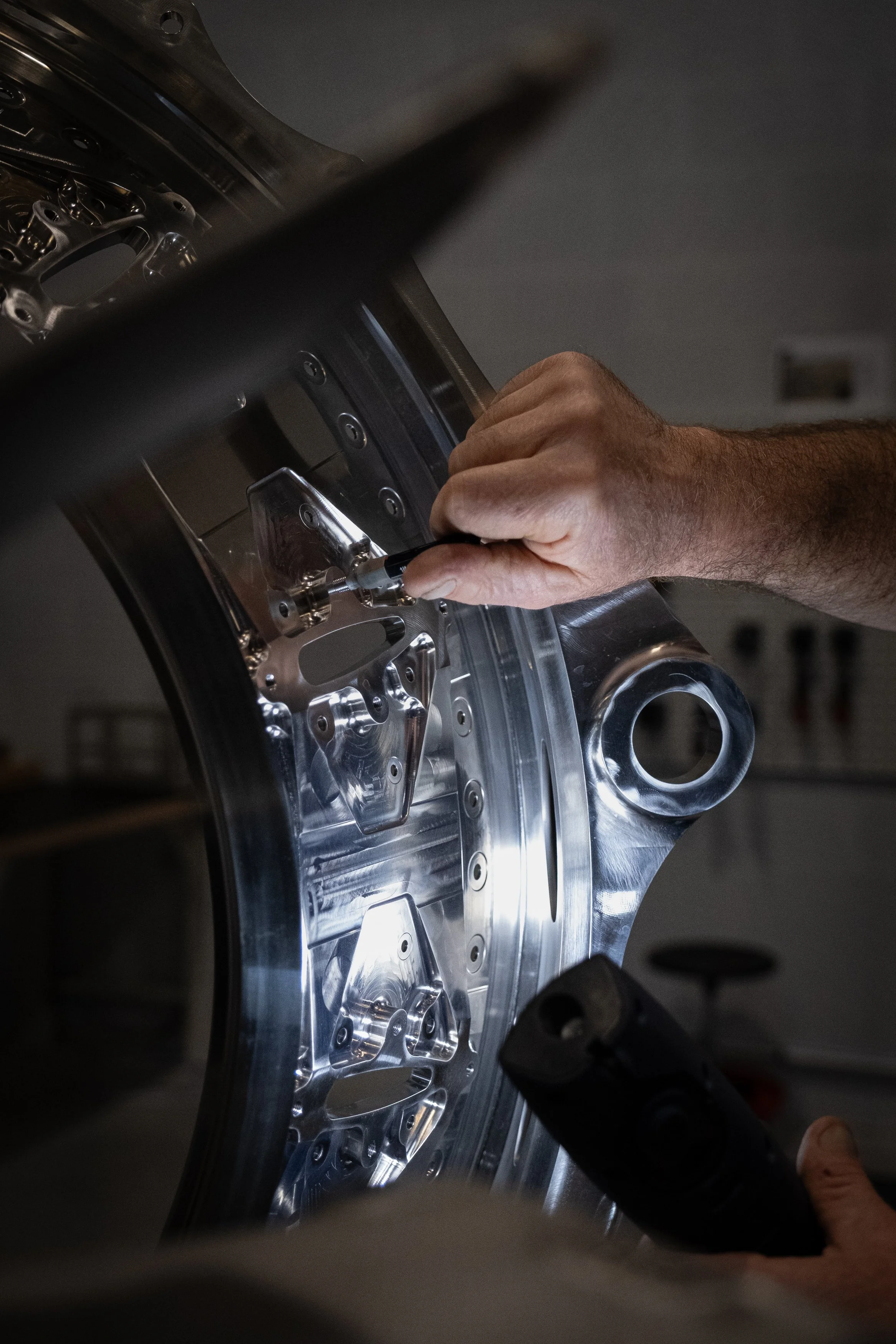 Une personne travaillant sur une pièce métallique brillante avec un tournevis et un outil électrique dans un atelier.