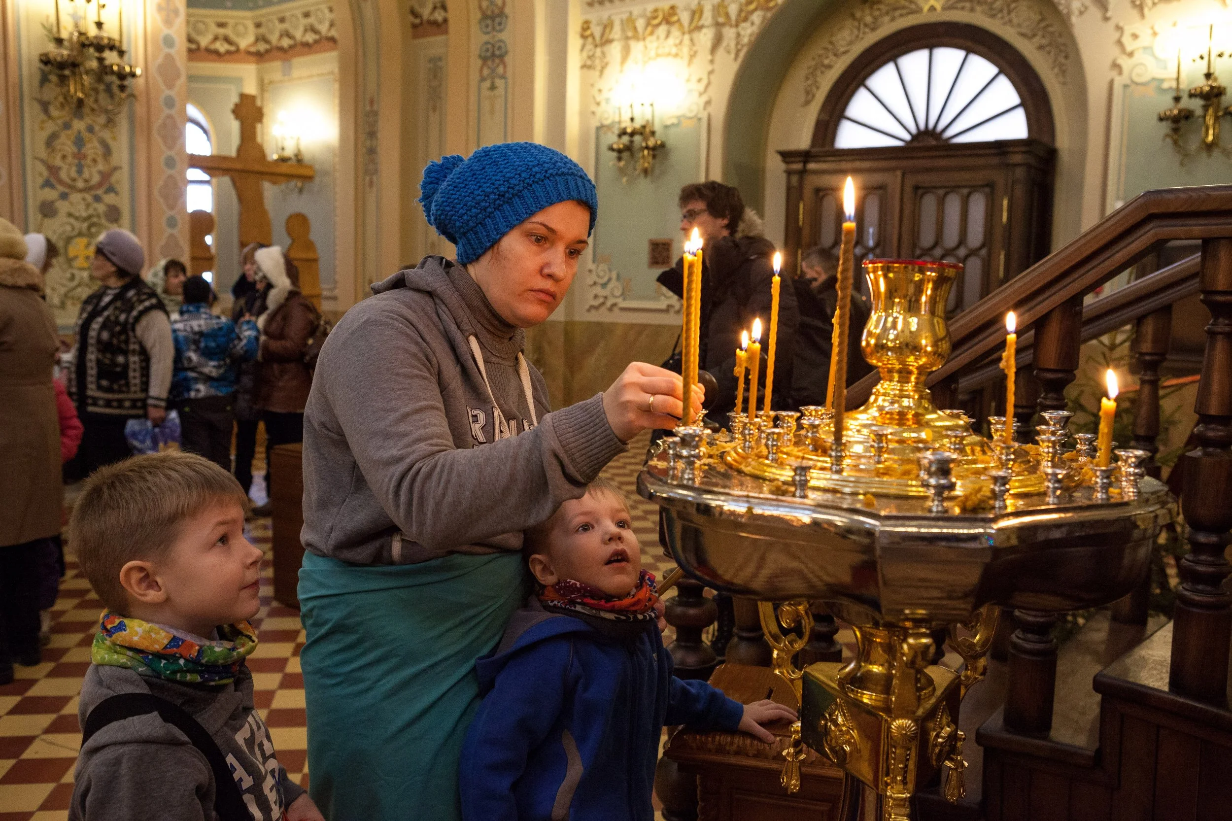 Une femme avec deux enfants dans une église avec des bougies allumées sur un candélabre en or.