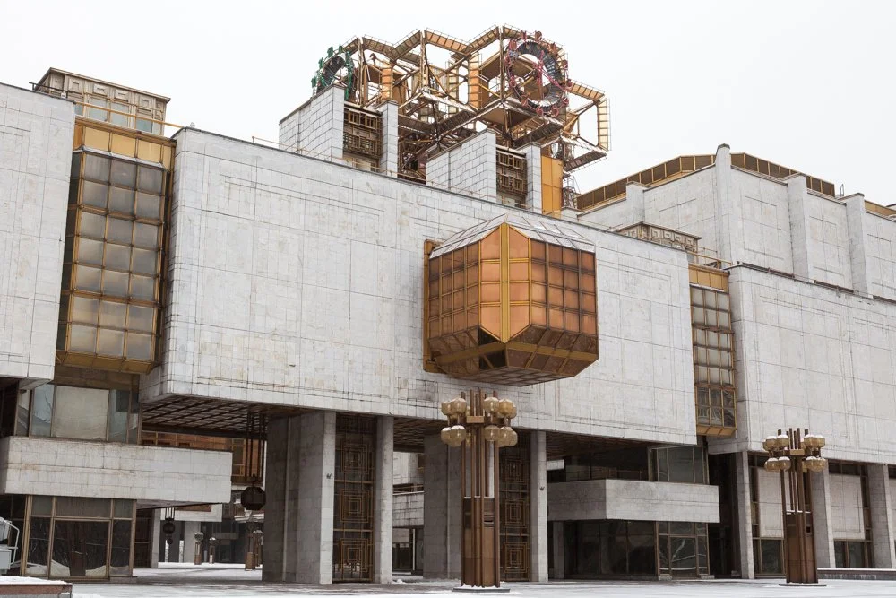 Bâtiment ancien avec une structure de style brutaliste et des éléments en cuivre, notamment une baie vitrée en forme de cube suspendu et des lampadaires rétro à Moscou.
