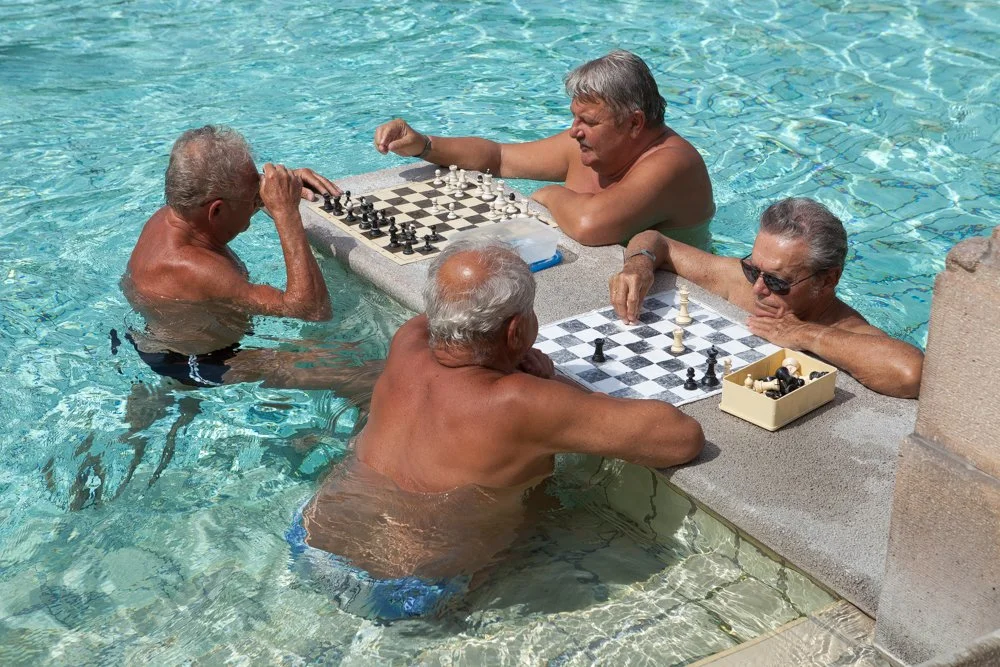Quatre hommes âgés jouent aux échecs dans la piscine des bains Szechenyi à Budapest en été.
