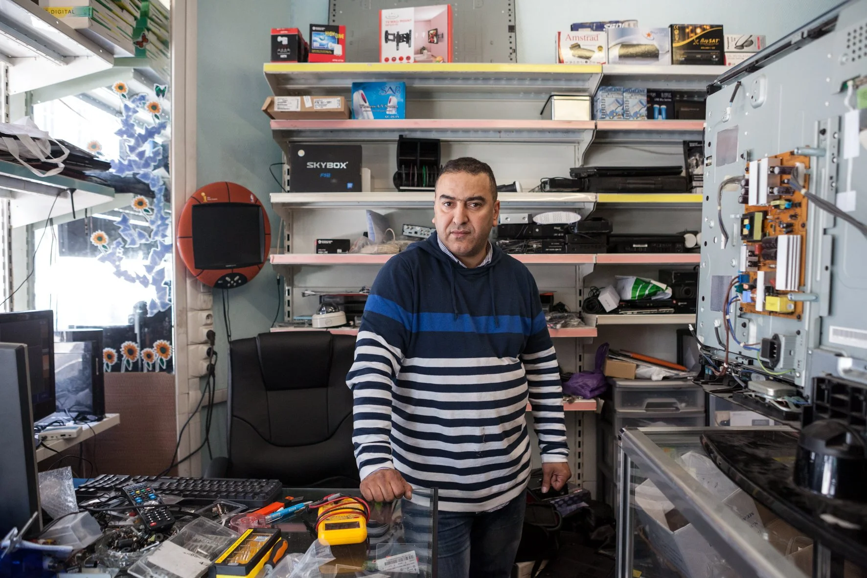 Un homme dans un atelier de réparation électronique, entouré d'outils et de composants électroniques sur un bureau.