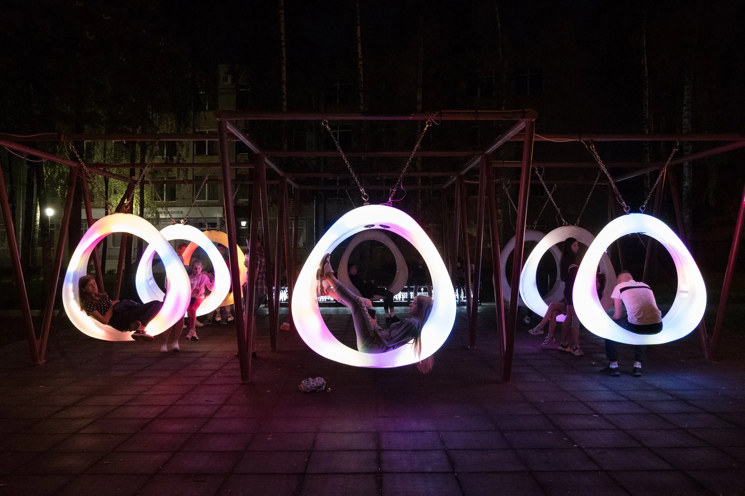 Jeux pour enfants avec cercles lumineux suspendus dans un parc en soirée à Minsk.