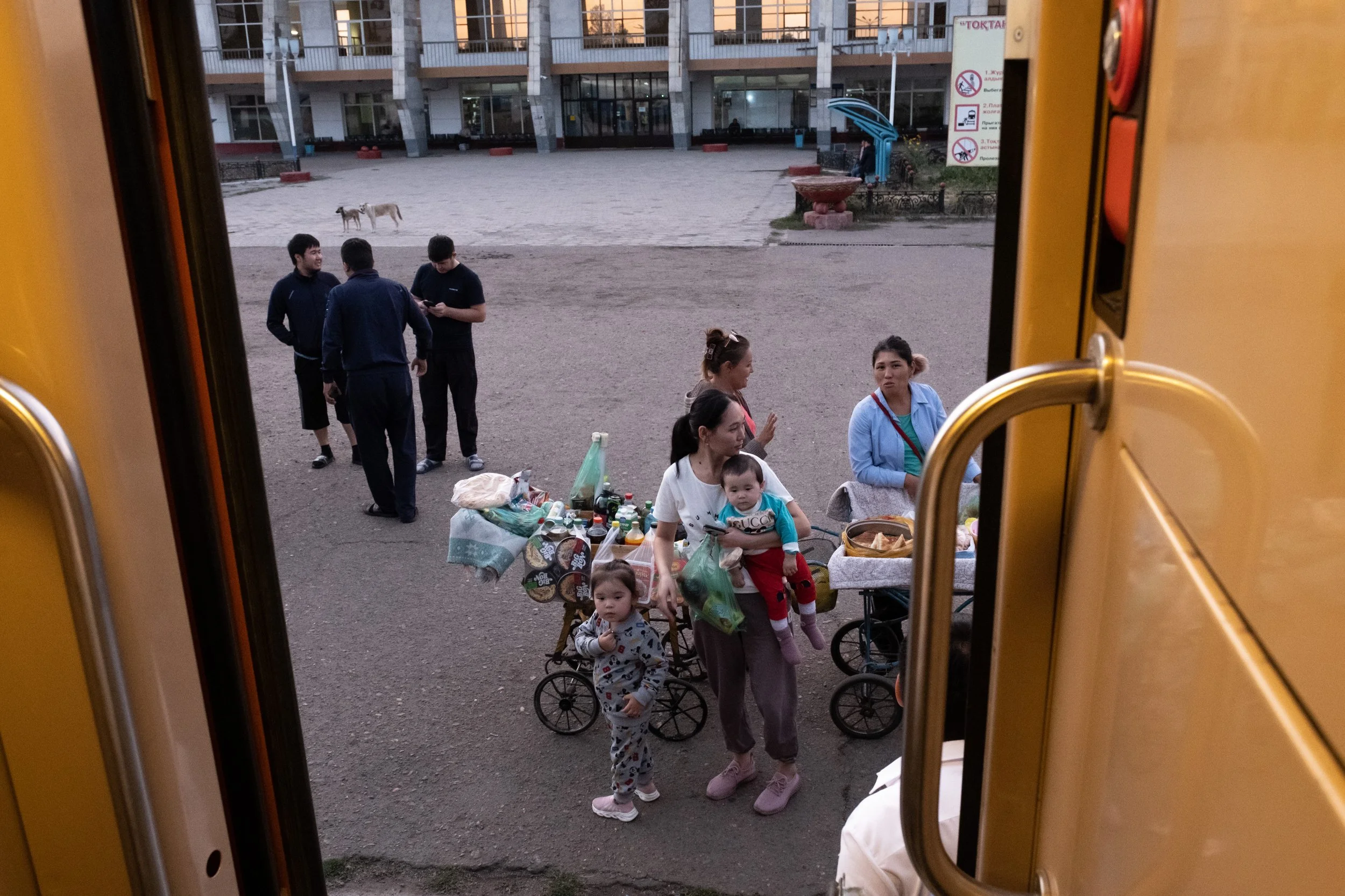Groupe de personnes sur le quai de la gare, vu depuis l'intérieur d'un train ouvert, avec un bâtiment en arrière-plan, au Kazakhstan.