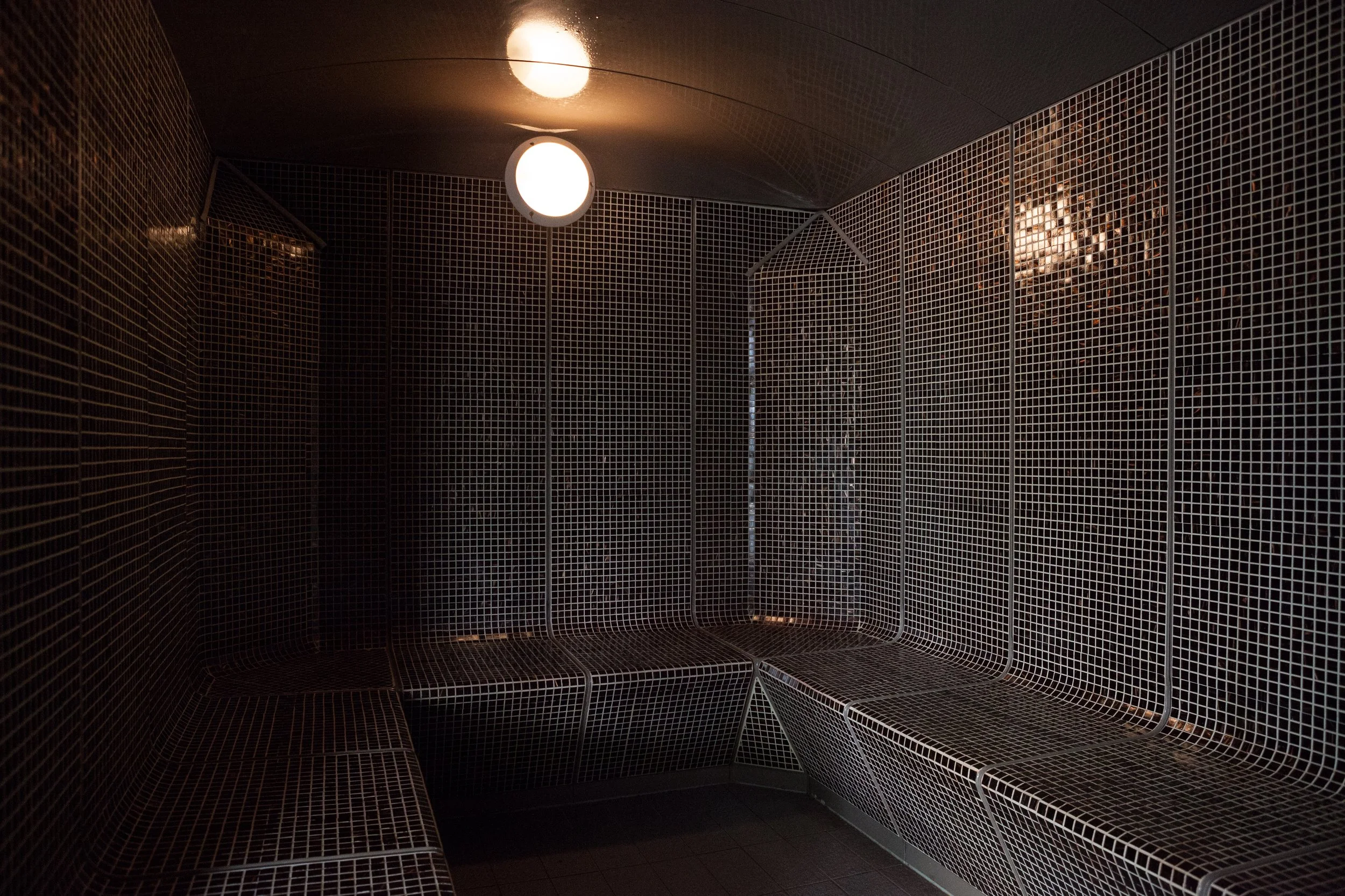 Cabine de sauna en mosaïque noire avec deux lampes au plafond.