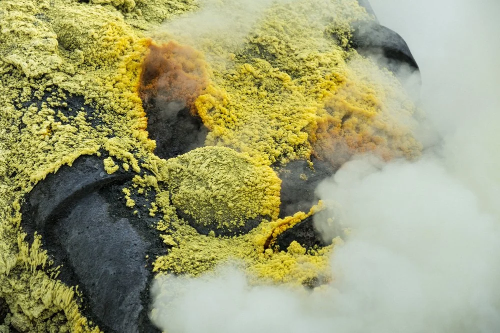 Cratère volcanique du volcan Ijen avec de la vapeur et des dépôts jaunes autour.
