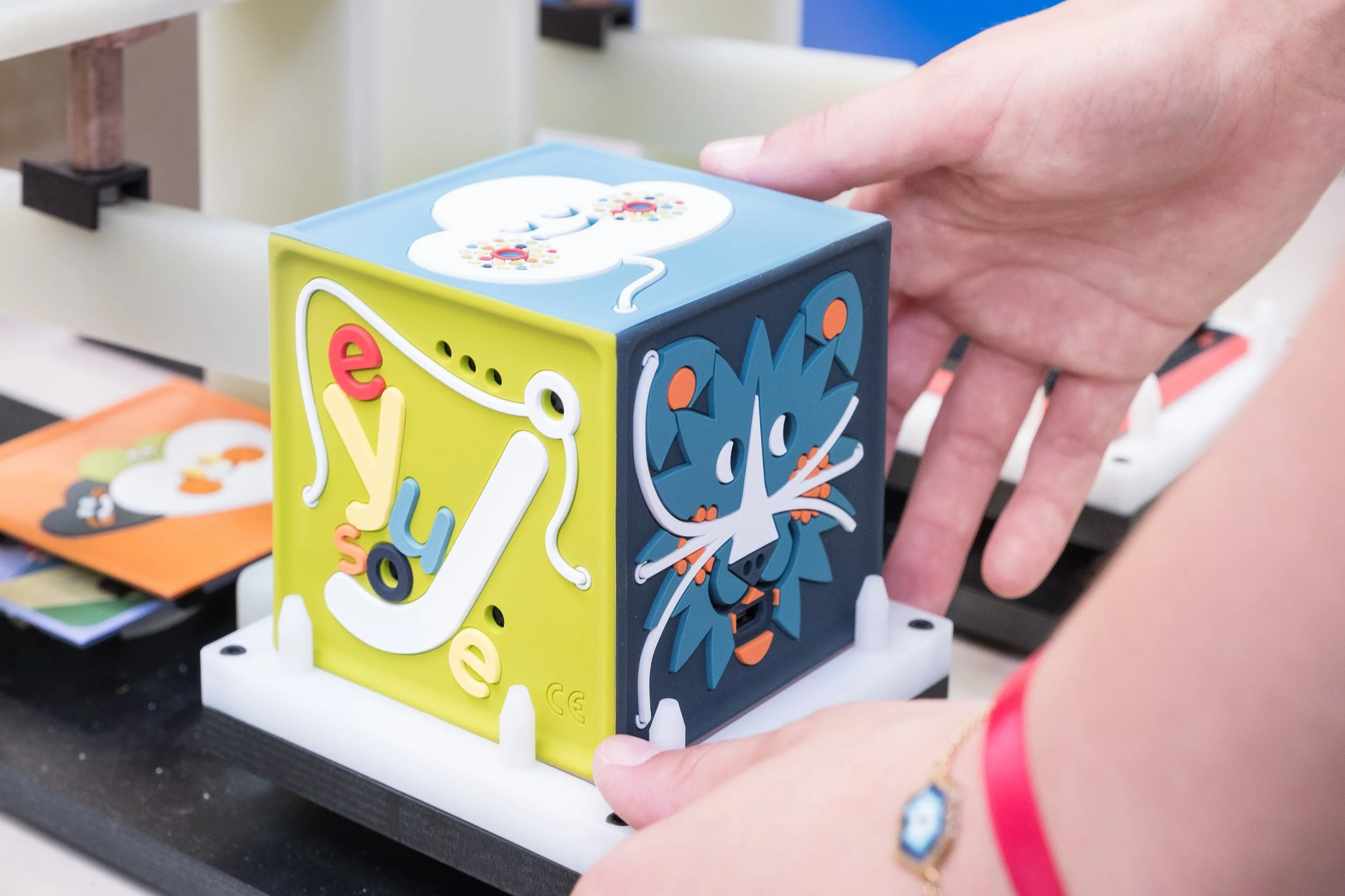 Une main manipule une conteuse colorée en forme de cube avec des illustrations de chiffres et de personnages.