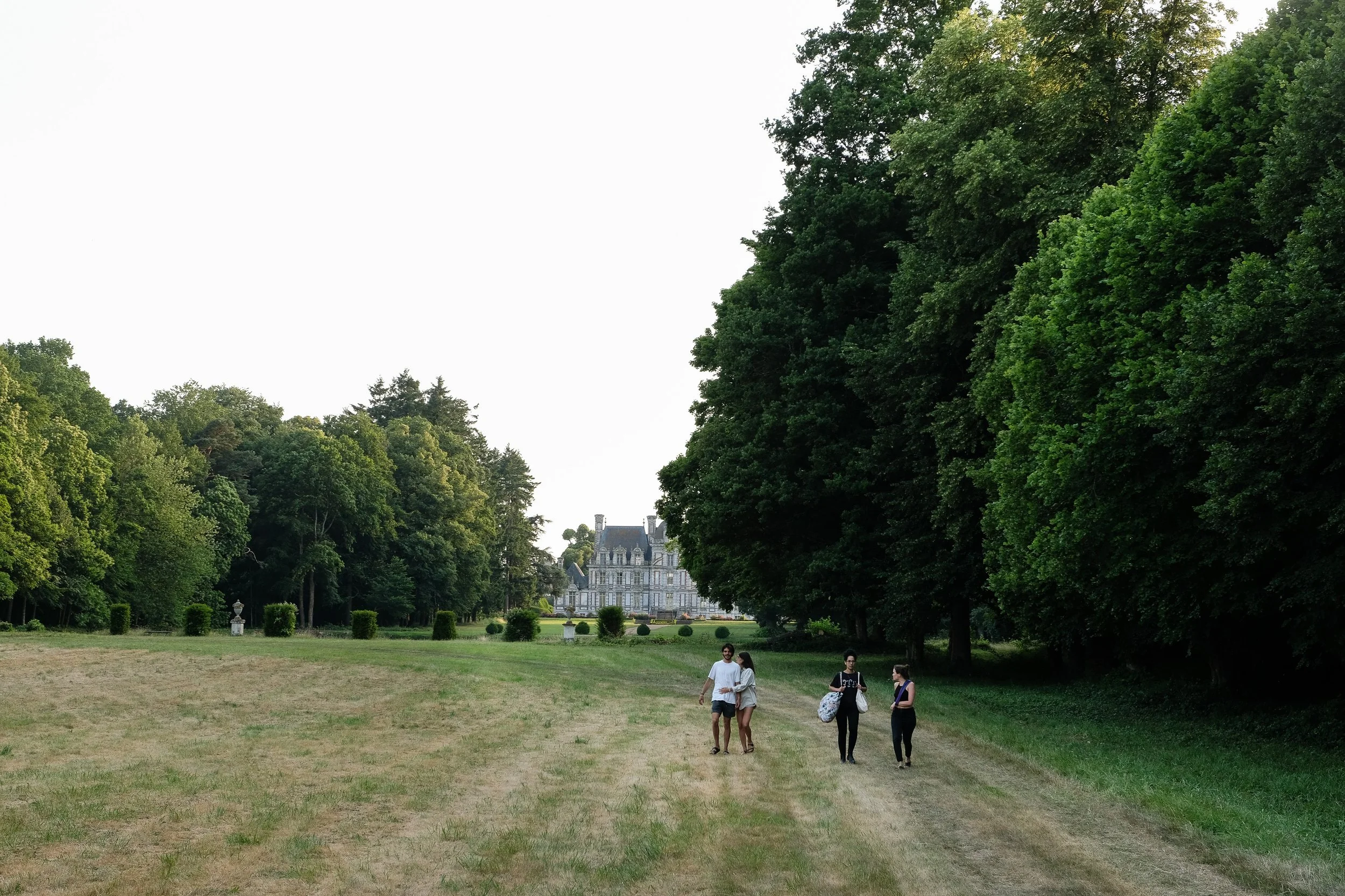Un groupe de quatre personnes marche sur un chemin sur une grande pelouse avec des arbres luxuriants et un château en arrière-plan.