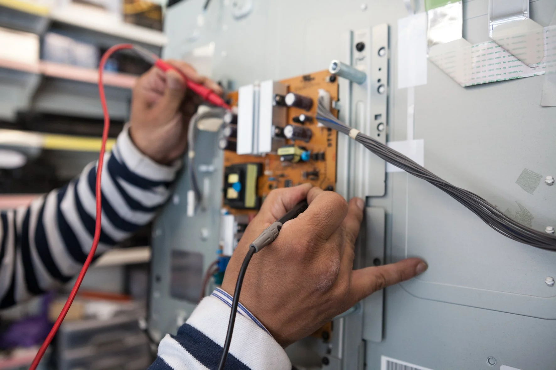 Un technicien répare un appareil électronique en manipulant une carte électronique, avec des outils de mesure et des câbles.