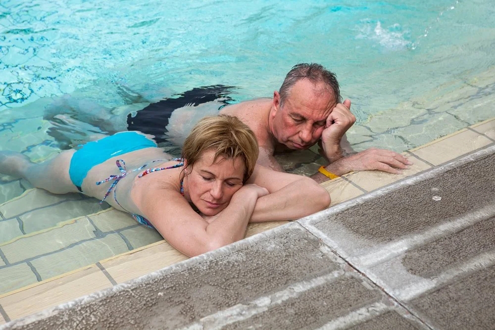 Un homme et une femme allongés sur le bord d'une piscine, tous deux appuyés sur leurs bras, assoupis.