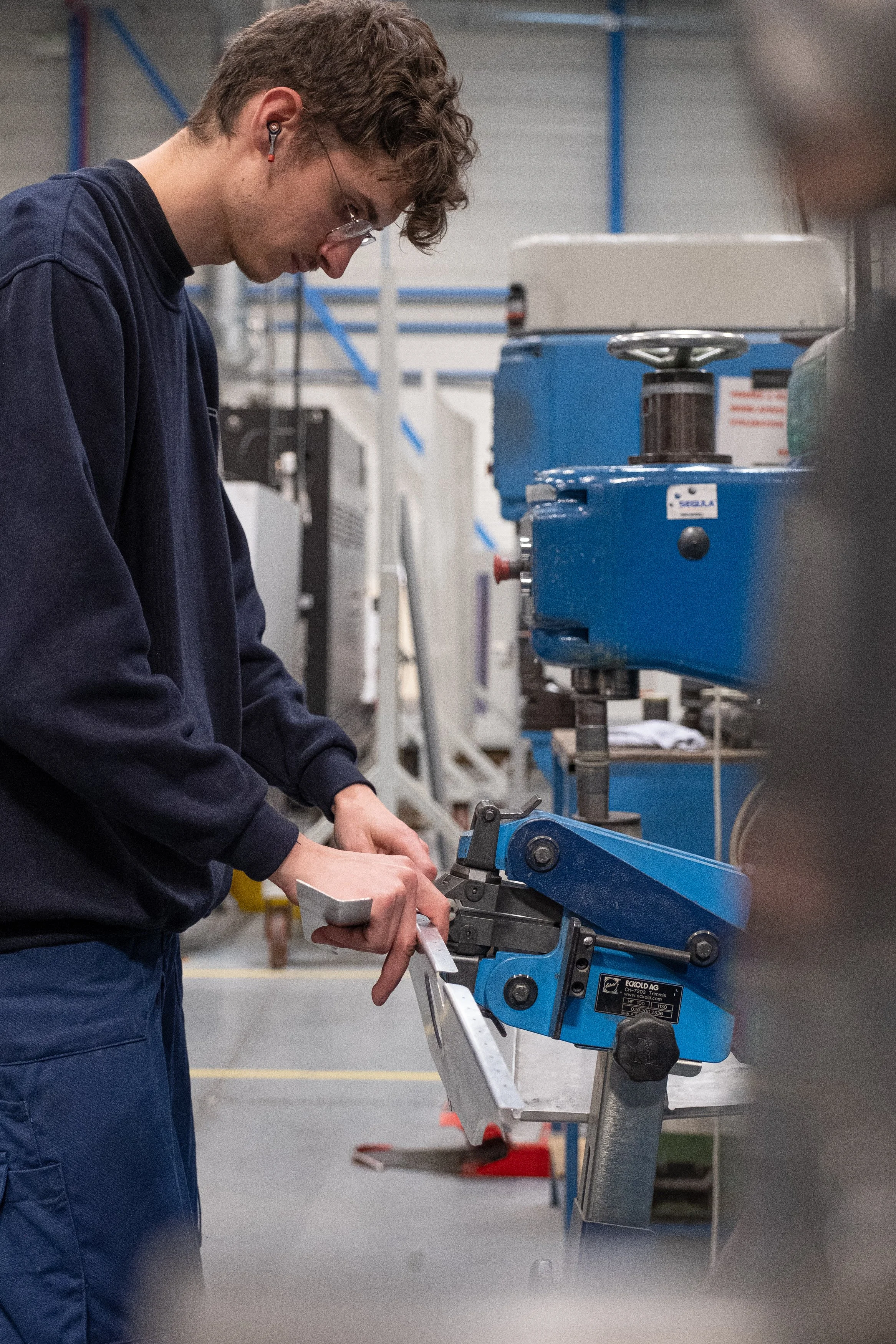 Jeune homme travaillant avec une machine-outil dans un atelier industriel.