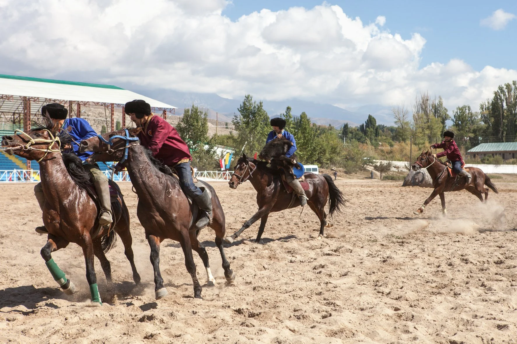 Groupe de cavaliers en compétition de kok boru sur un terrain en sable, portant des vêtements traditionnels avec chapeaux en fourrure.