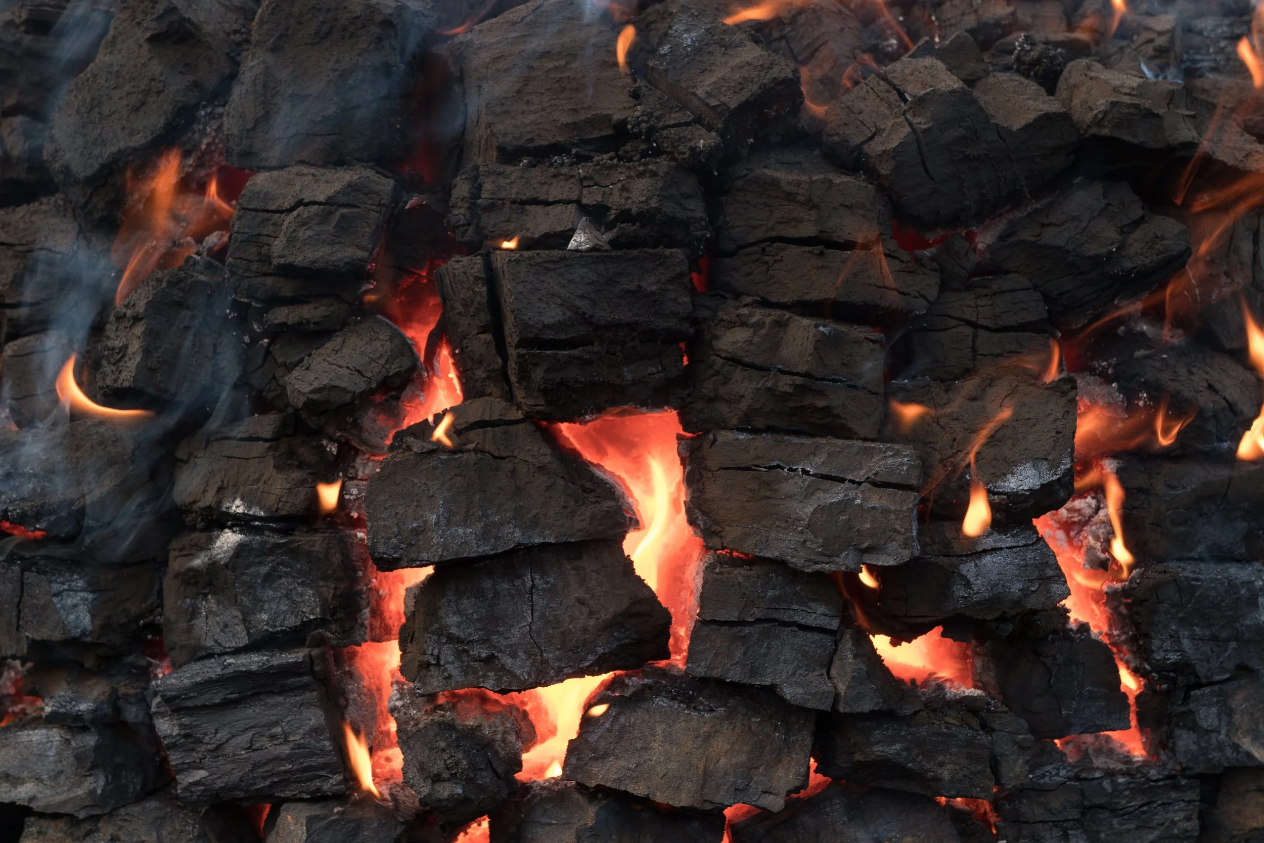 Charbon de bois en combustion, avec des flammes orange et une lueur rougeâtre entre les morceaux