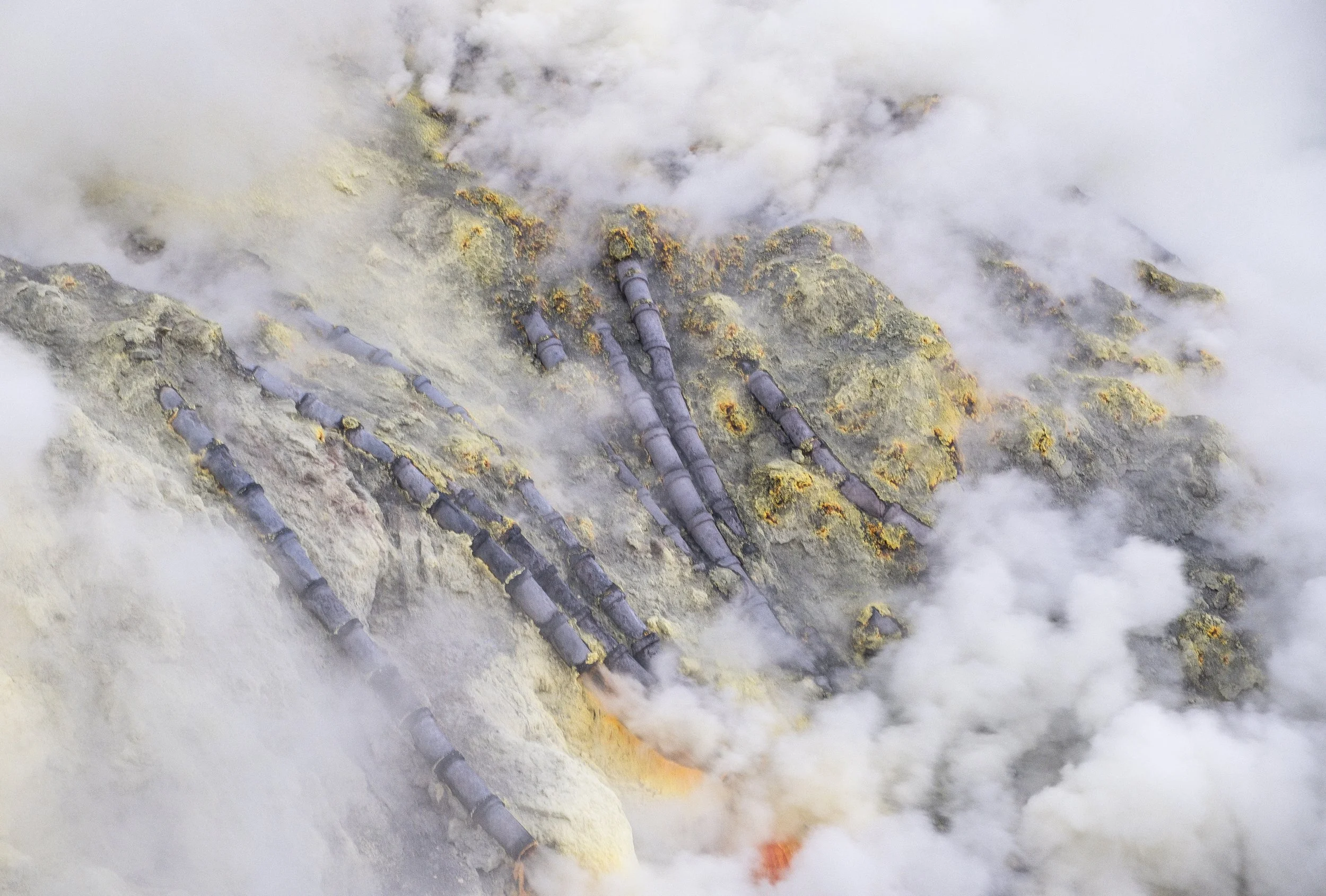 Fumerolles de vapeur qui s'échappent de la surface d'une zone géothermique avec des tuyaux noirs traversant la roche.