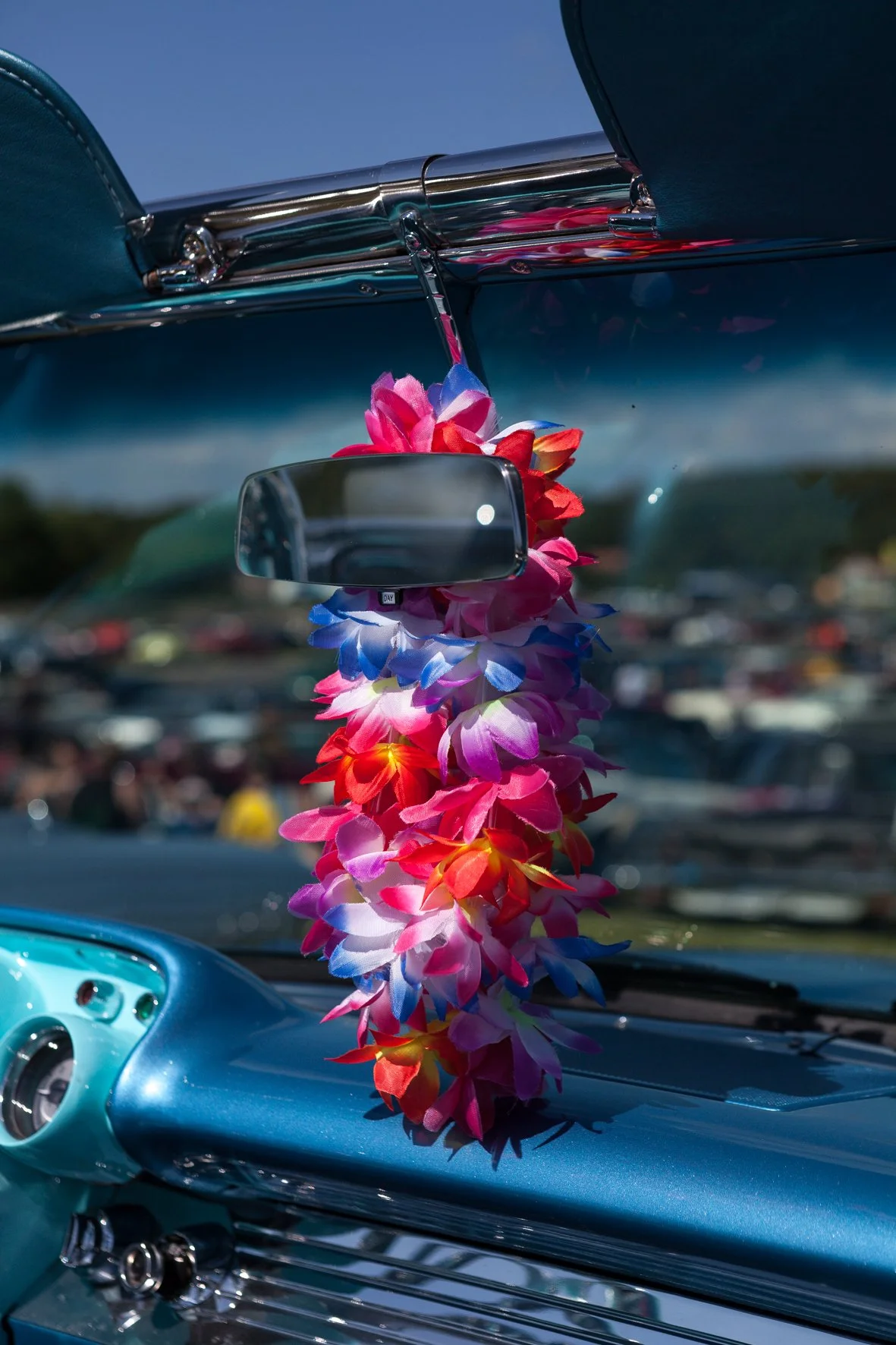 Un tableau de bord de voiture vintage avec un décor de colliers de fleurs colorés suspendus au miroir.