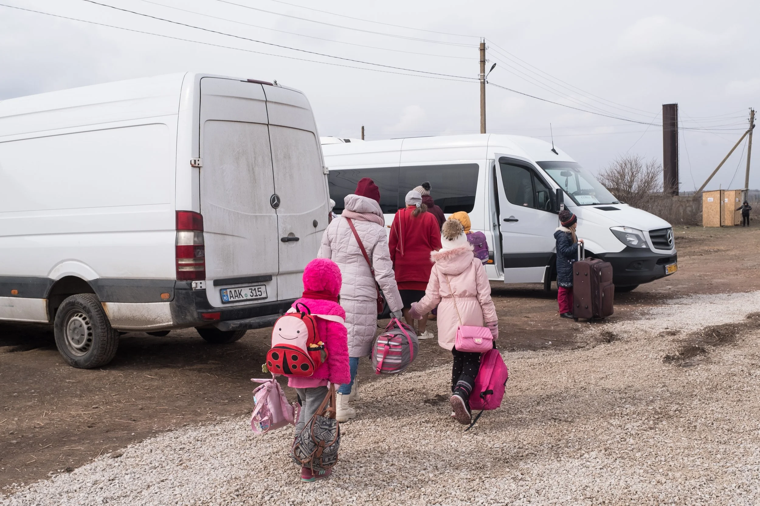 Groupe de réfugiés ukrainiens, dont plusieurs enfants, allant vers une navette dans une zone de stationnement extérieure, par temps froid.