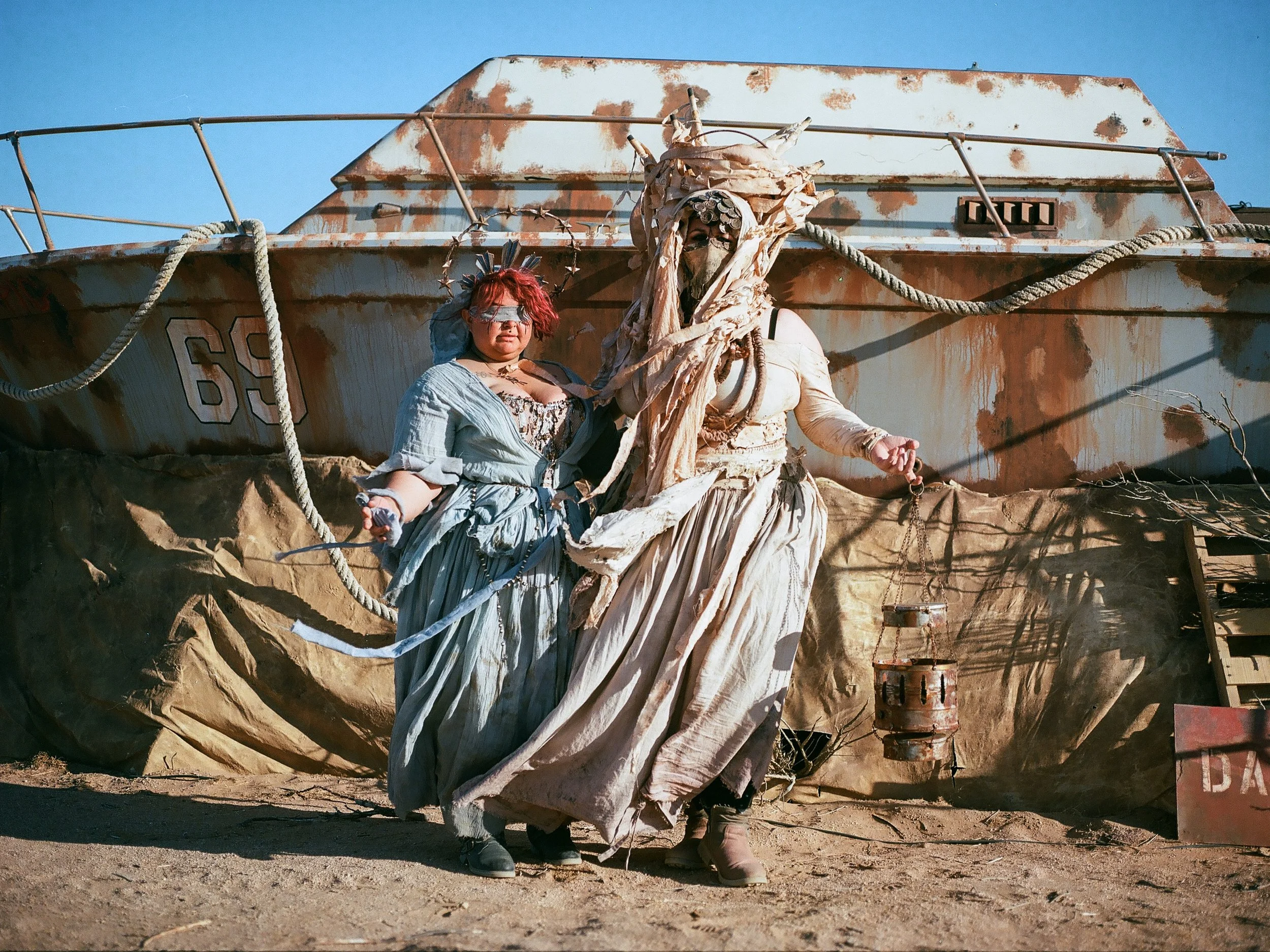 Deux personnes déguisées en costumes post-apocalyptiques debout devant un bateau rouillé dans un environnement désertique à Wasteland.