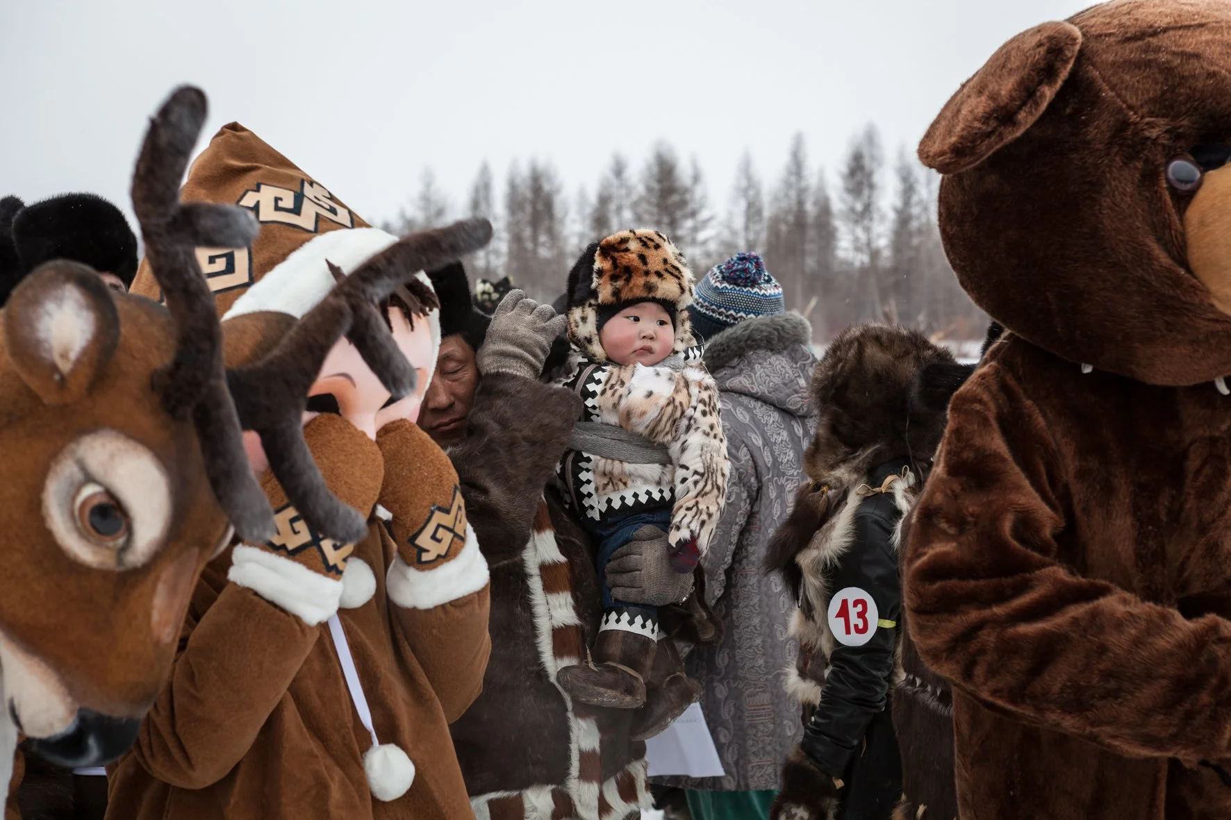 Enfants et adultes déguisés en animaux, notamment rennes, ours et jaguars, lors d'un événement en extérieur durant l'hiver, avec un fond d'arbres et un ciel nuageux.
